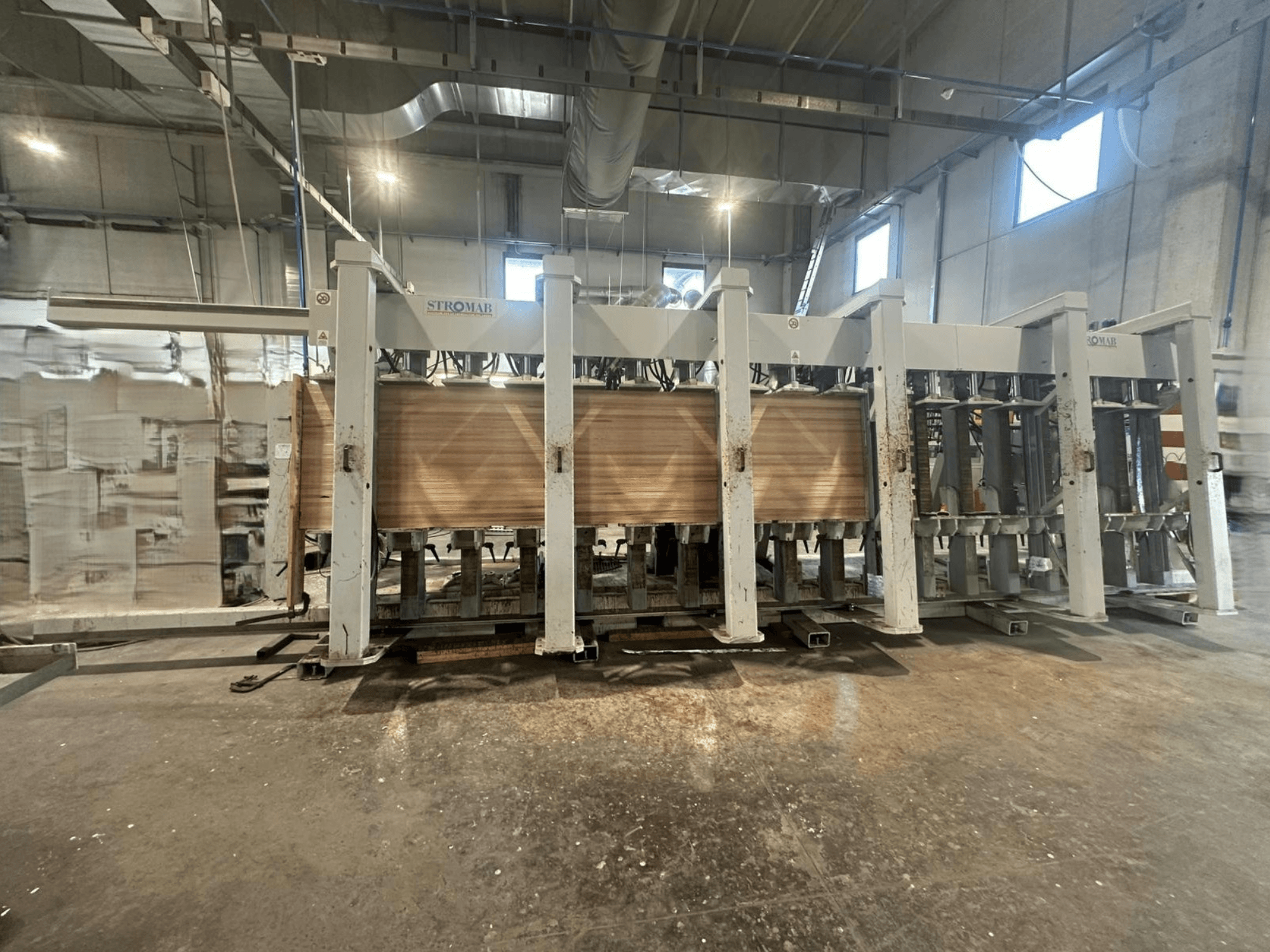 Bir depoda endüstriyel STROMAB makinesi, önden görünüm, ahşap paneller işleniyor, metal yapı ve mekanik parçalar sergileniyor.