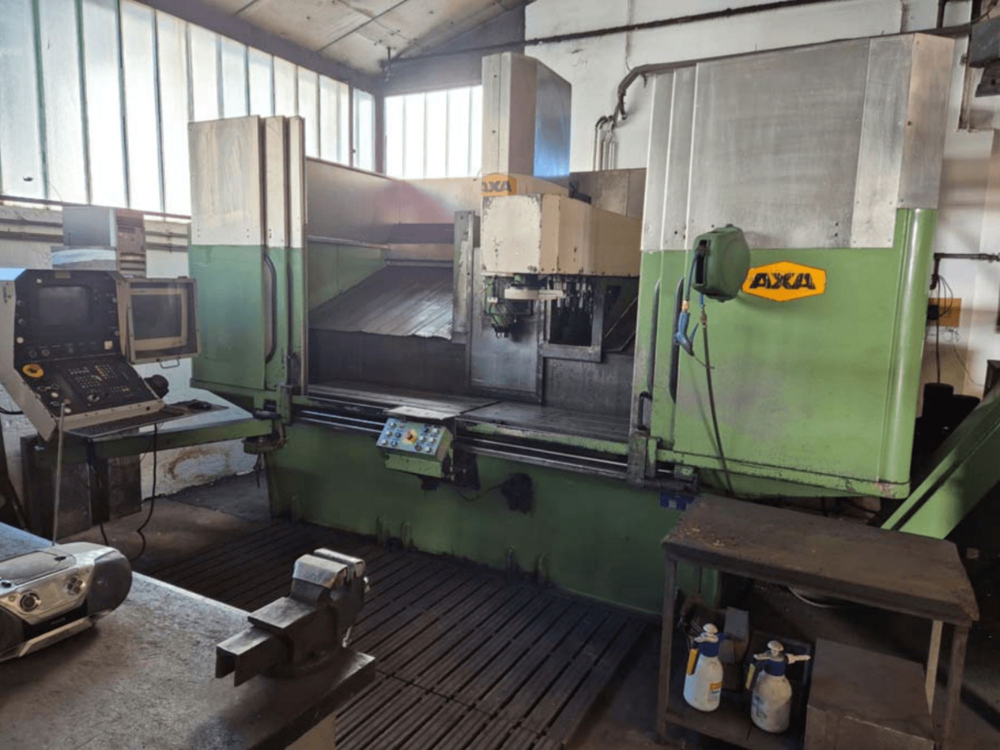 AXA VSC-2M dikey işleme merkezi, önden görünüm, kontrol paneli ve kesme takımları ve temizlik malzemeleri içeren çalışma alanı.