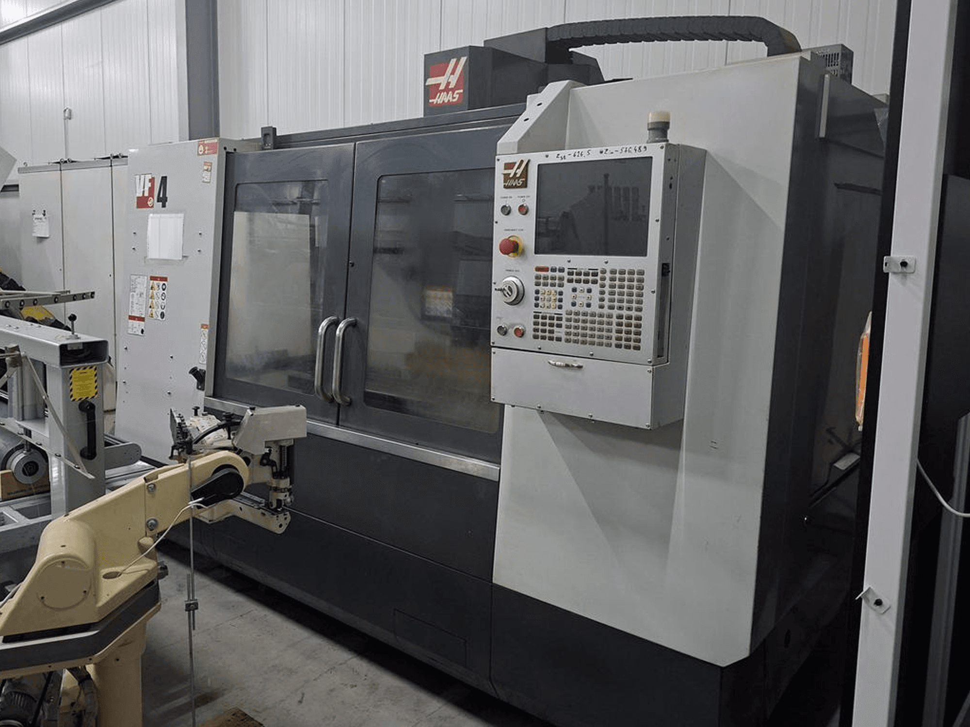 Haas VF-4 CNC freze makinesinin önden görünümü, sayısal kontrol paneli ve otomasyon için robotik kola sahiptir.
