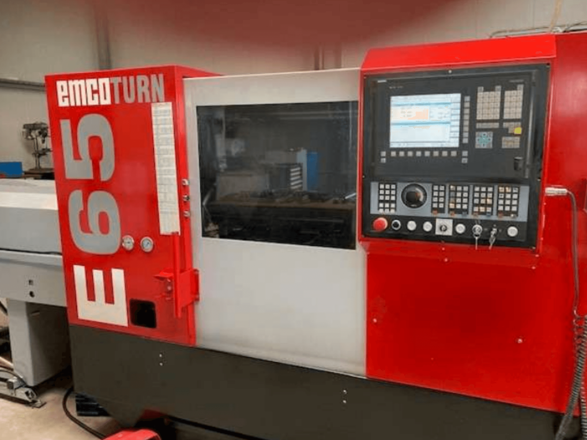 EMCO Turn E65 CNC torna tezgahı, kontrol panelini, büyük ekranı ve camın arkasındaki çalışma alanını gösteren önden görünüm.