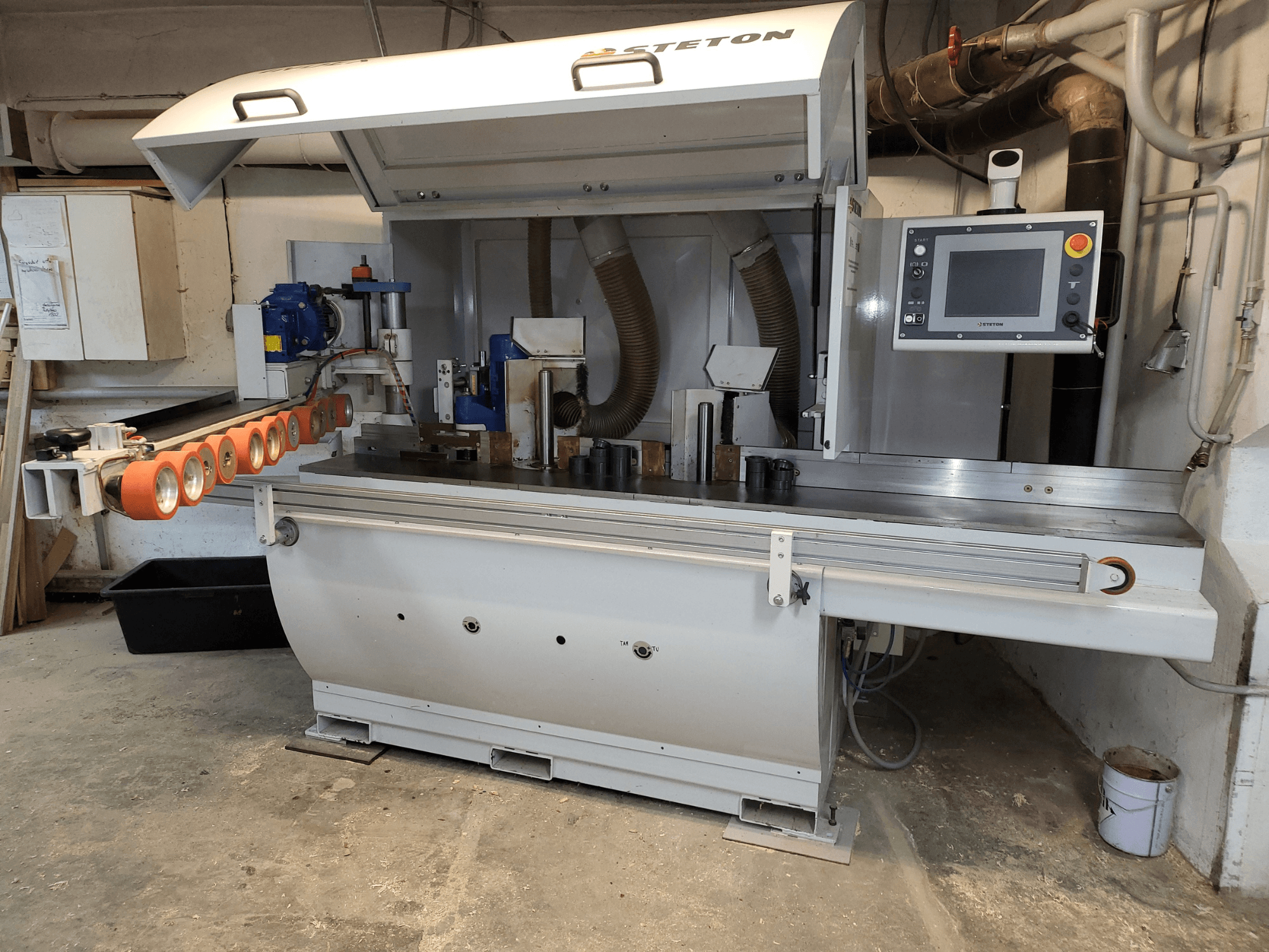 Kontrol paneli, besleme boruları ve masanın üzerinde çeşitli ahşap parçaları bulunan bir Stetton ahşap işleme makinesinin önden görünümü.