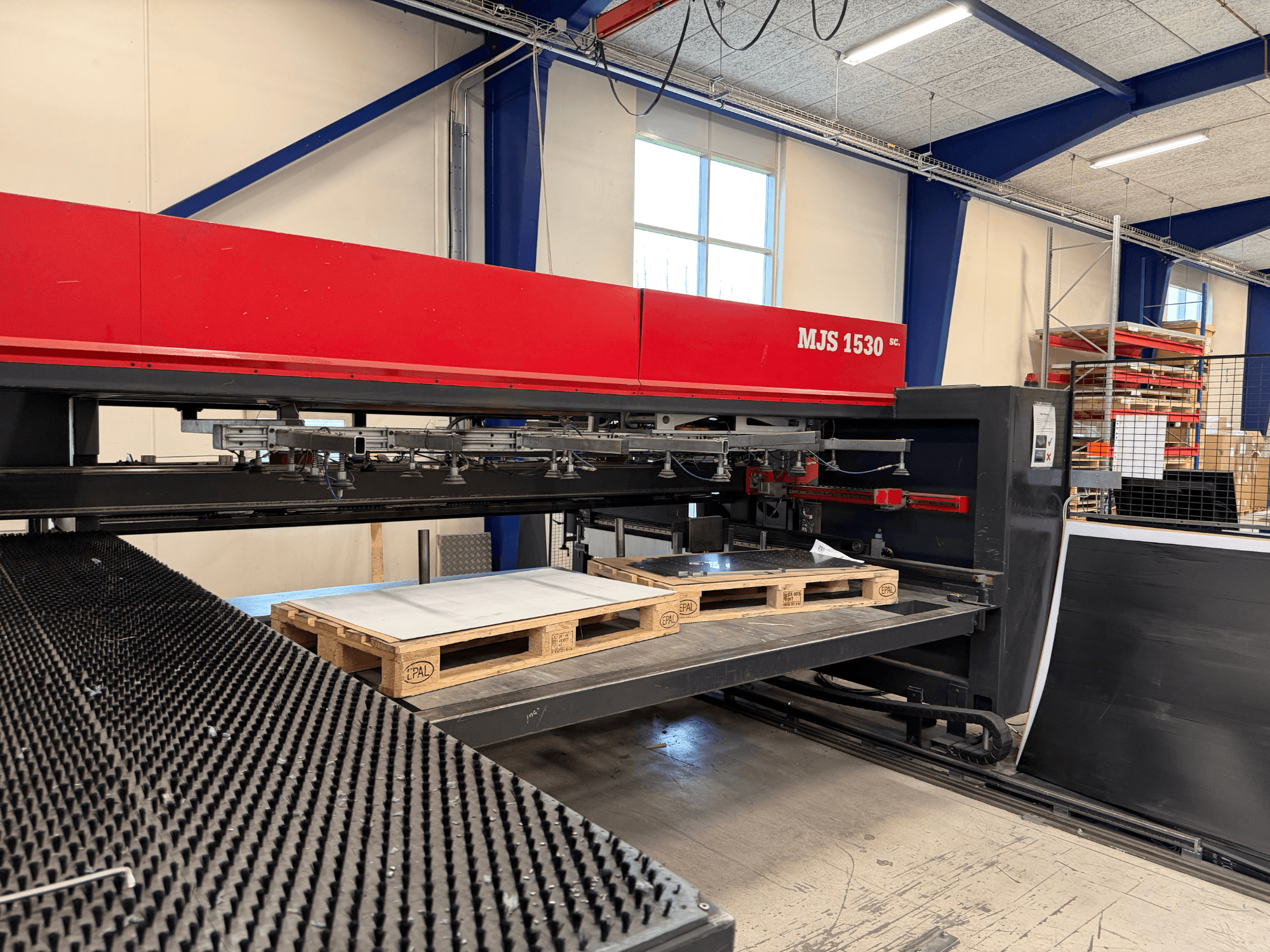 Bir atölyede MJS 1530 CNC makinesi, önden görünüm, yükseltilmiş bir platform üzerinde bir metal levha tutan ahşap bir palet ile.