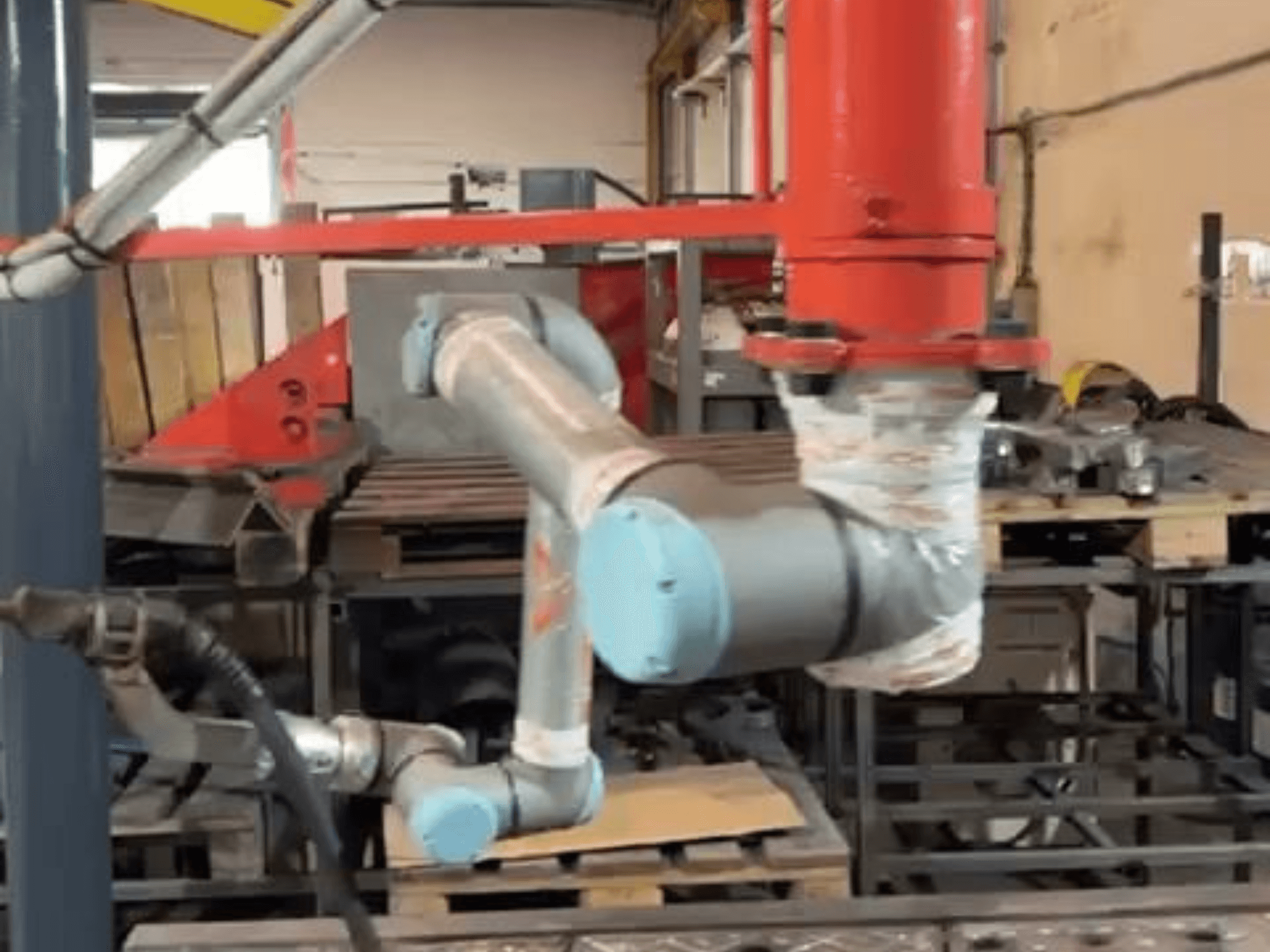 Bir atölyede bulunan Universal Robots UR10e işbirlikçi robot; makinelerin yakınında kol ve eklem hareketlerini gösteren yandan görünüm.