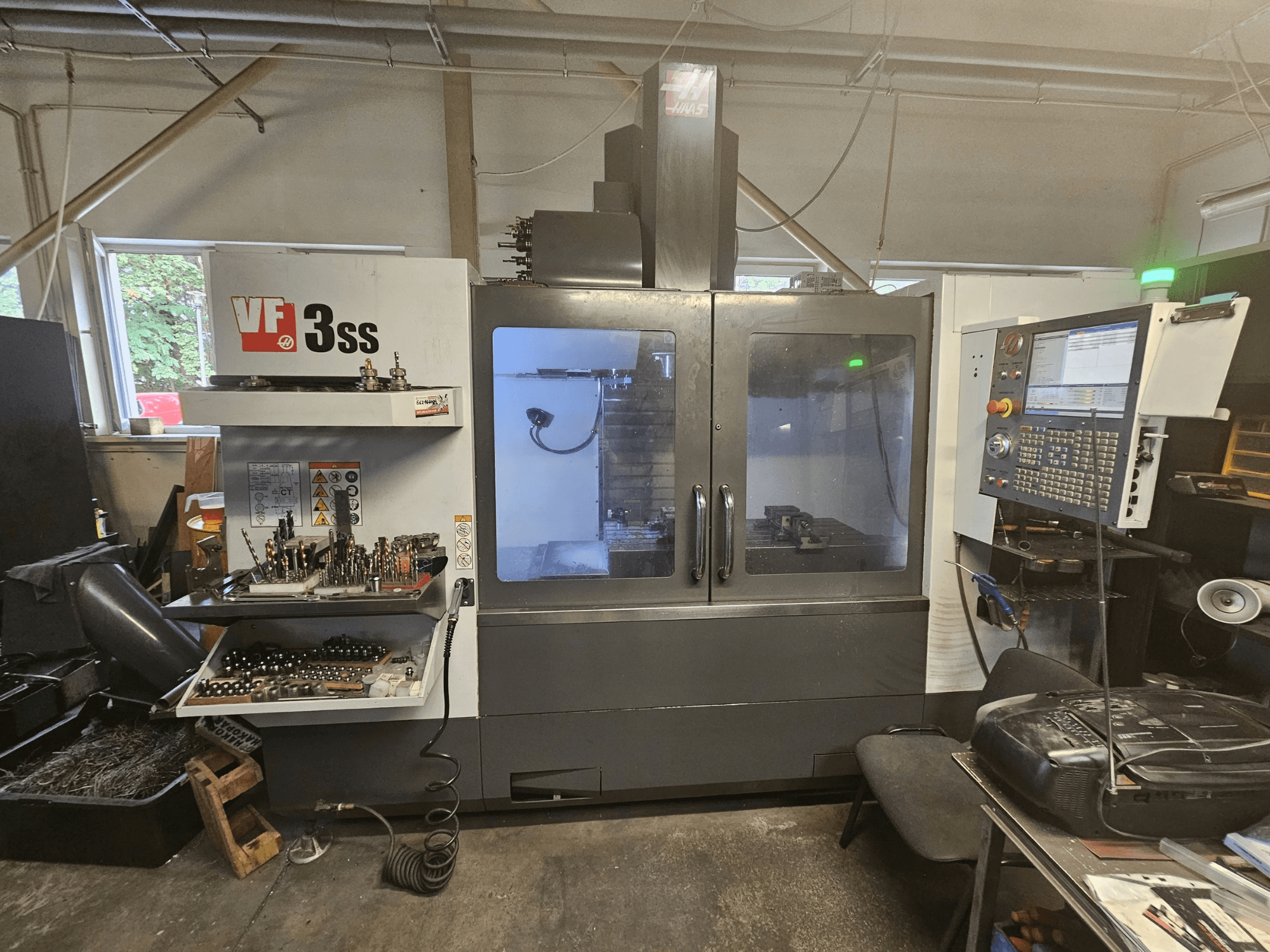 Bir atölyede bulunan Haas VF-3SS dikey işleme merkezi; kontrol paneli ve takım saklama bölmesini gösteren önden görünüm.