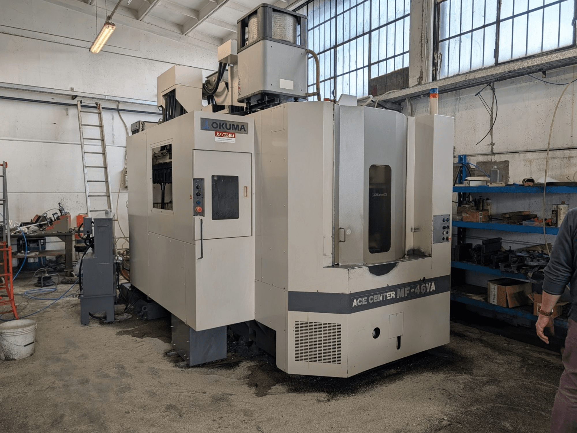 Okuma ACE CENTER MF-46VA dik işleme merkezi atölyede, kontrol paneli ve çevresindeki ekipmanlarla önden görünüm.
