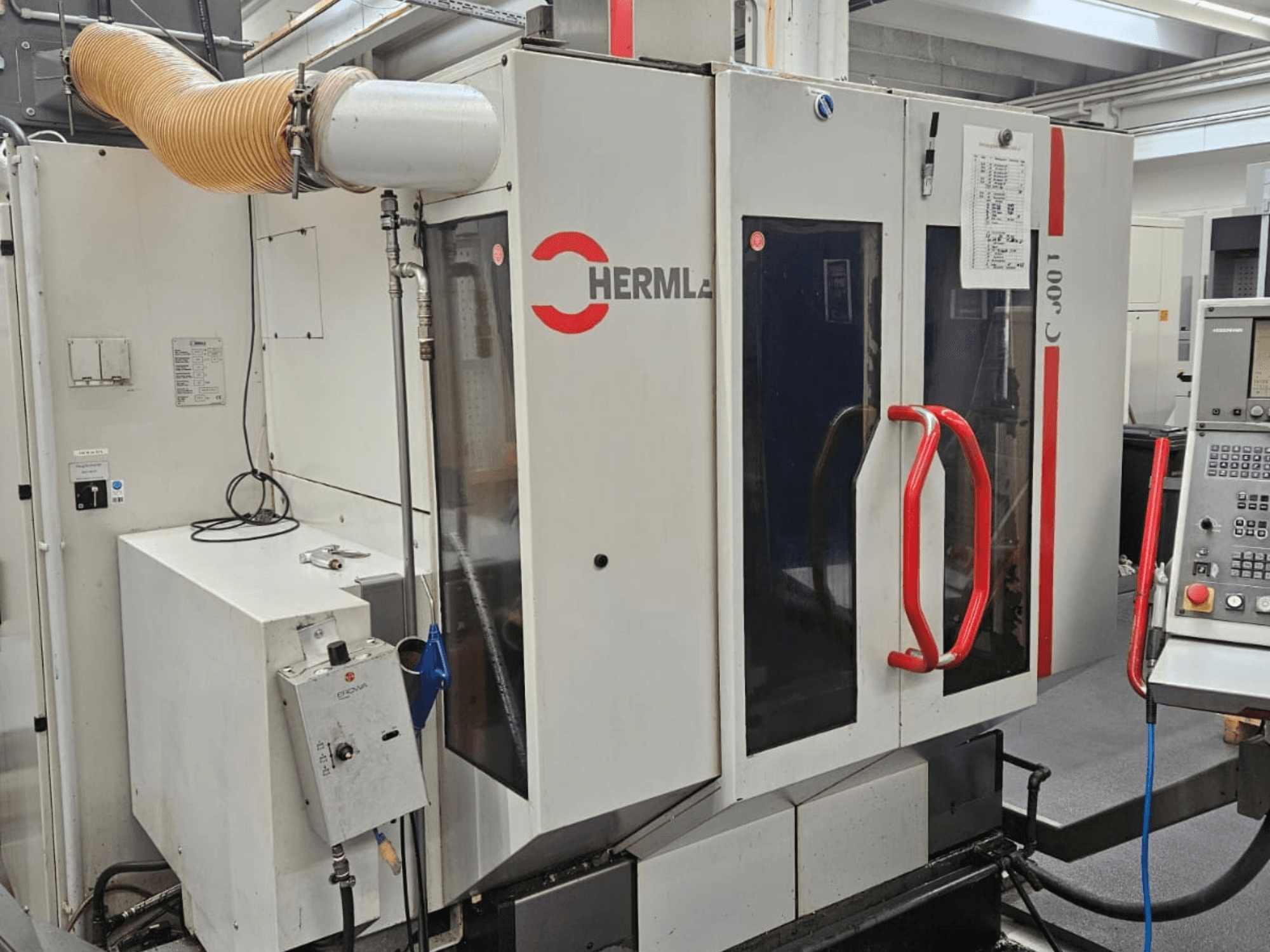 HERMLE C 600 U üniversal işleme merkezinin önden görünümü, kontrol panelini ve kapılardaki kırmızı tutamakları gösterir.