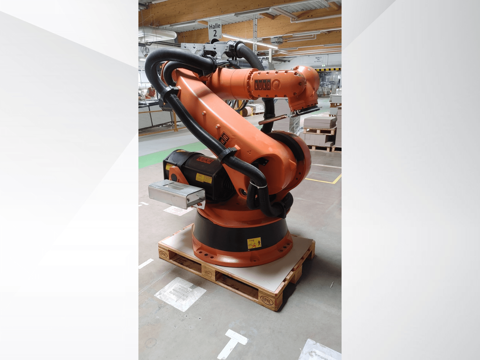 Turuncu renkli KUKA KR140-3 COMP robot kolu, ahşap bir palet üzerinde önden görünüm, kavisli bir kol ve kontrol kutusu.