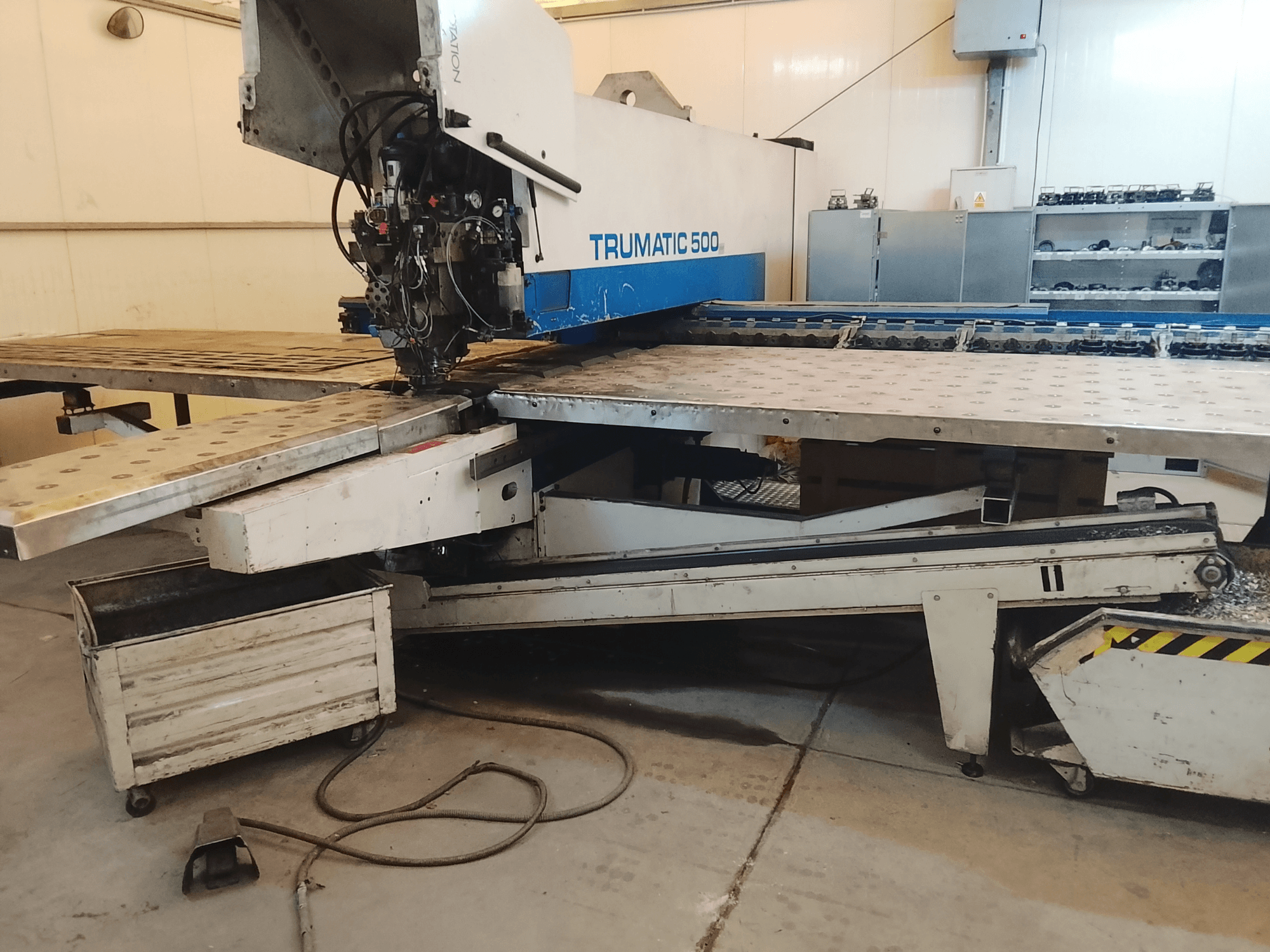 Atölyedeki TRUMATIC 500 CNC makinesi, kesme kafasını ve önceden delinmiş deliklere sahip metal çalışma tablasını gösteren yandan görünüm.