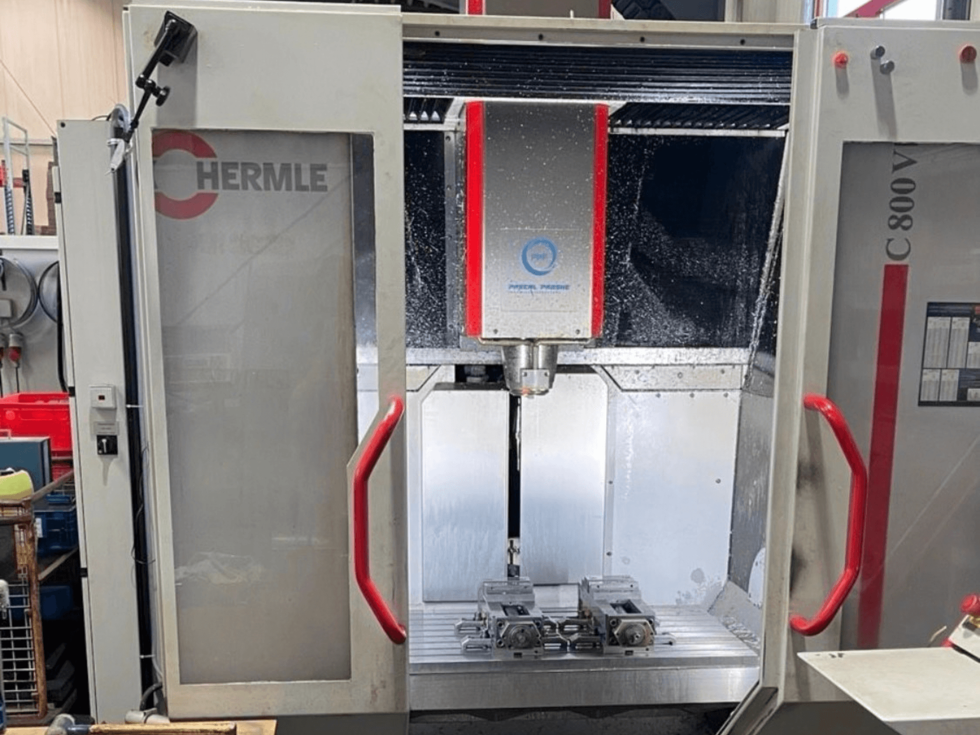 HERMLE C800V dikey işleme merkezi; iş parçaları ve sıvı soğutma sıvısının bulunduğu işleme alanını gösteren önden görünüm.