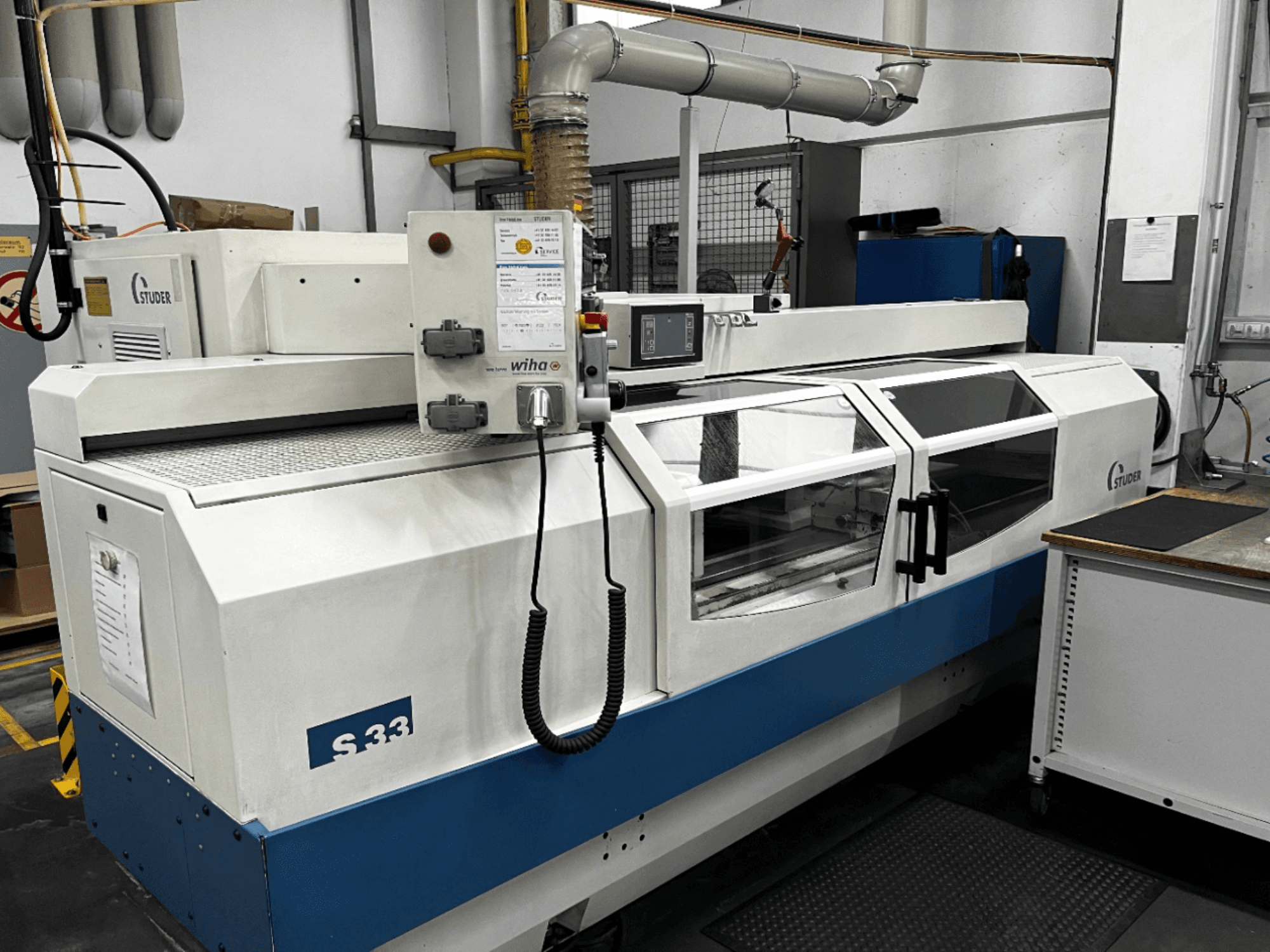 STUDER S33 CNC silindirik taşlama makinesi, önden görünüm; kontrol paneli ve cam güvenlik kapılarına sahiptir. Endüstriyel ortam.