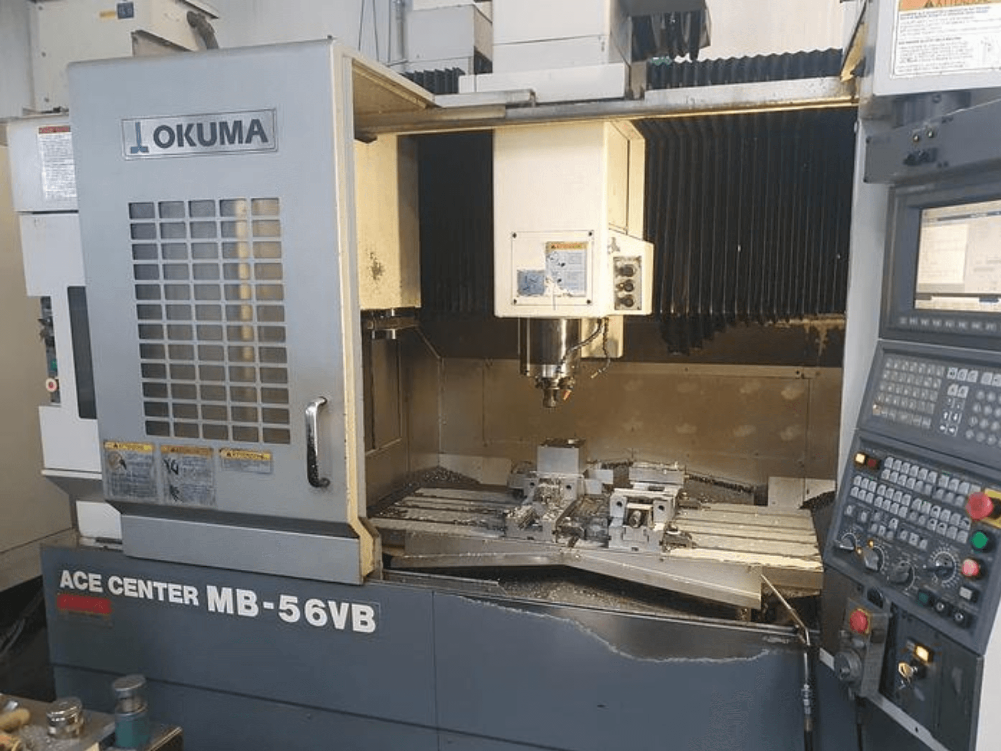 Okuma ACE CENTER MB-56VB CNC freze makinesinin önden görünümü, kontrol panelini ve işleme alanını göstermektedir.