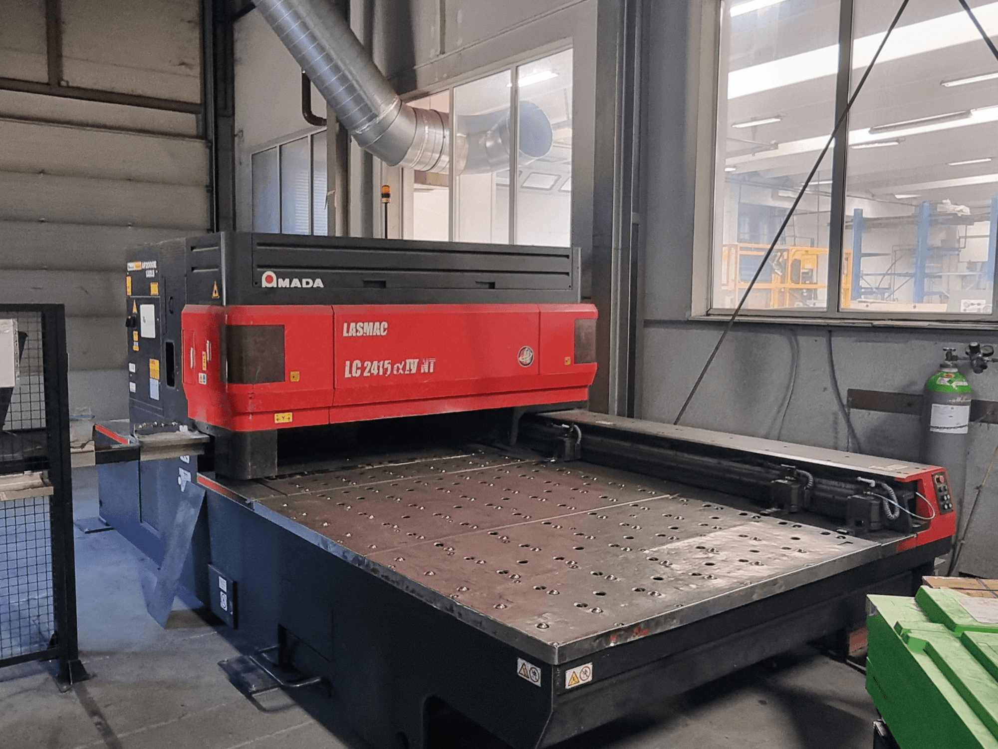 Amada LASMAC LC 2415 αⅡ NT lazer kesim makinesi, kırmızı ve siyah, önden görünüm, motorlu kesim yatağı ve hassas kontroller.