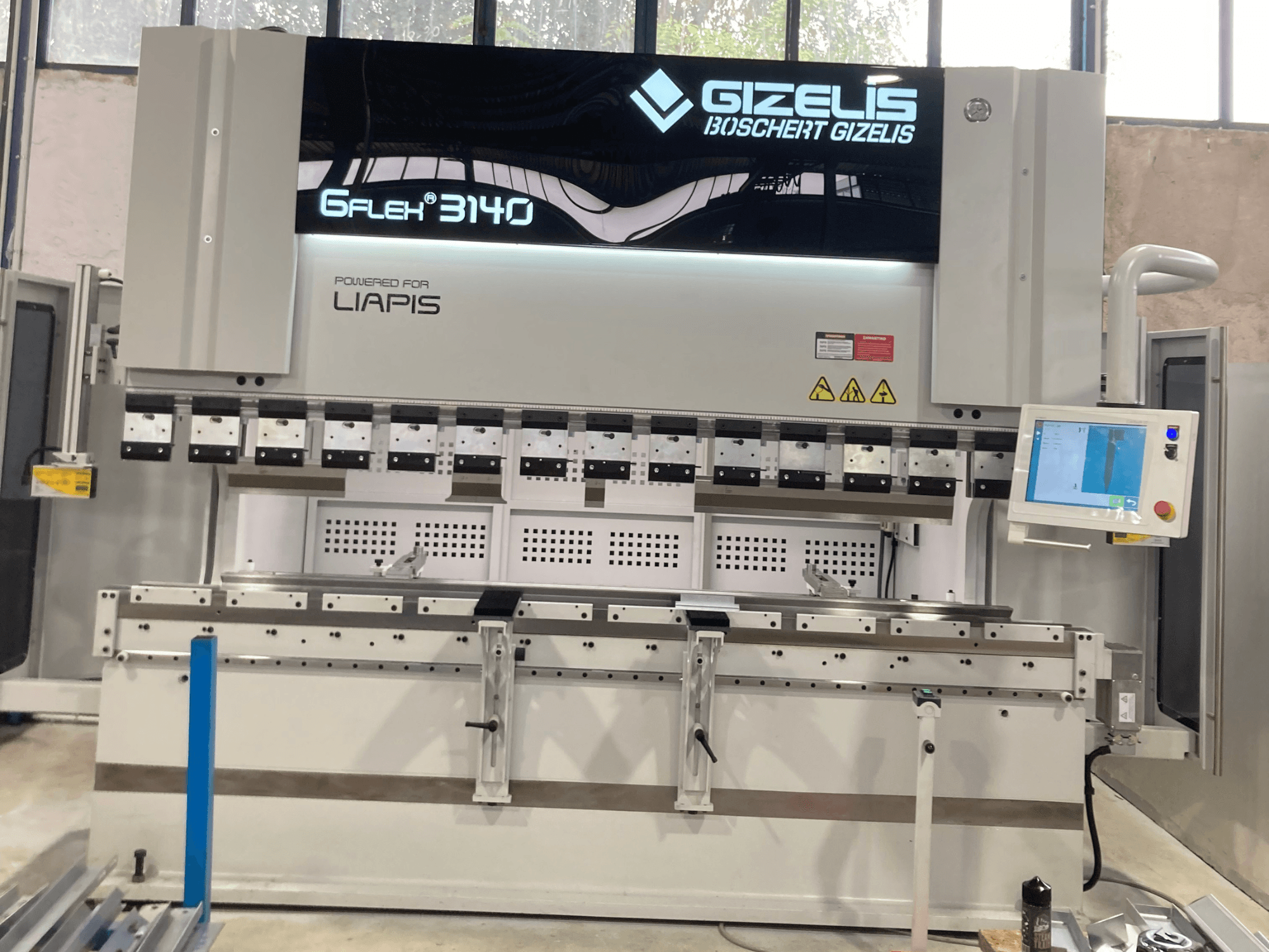 Hidrolik pres GIZELIS G-FLEX 3140, kontrol ekranı ile önden görünümde, çoklu bükme aletleri ve güvenlik etiketleri ile.