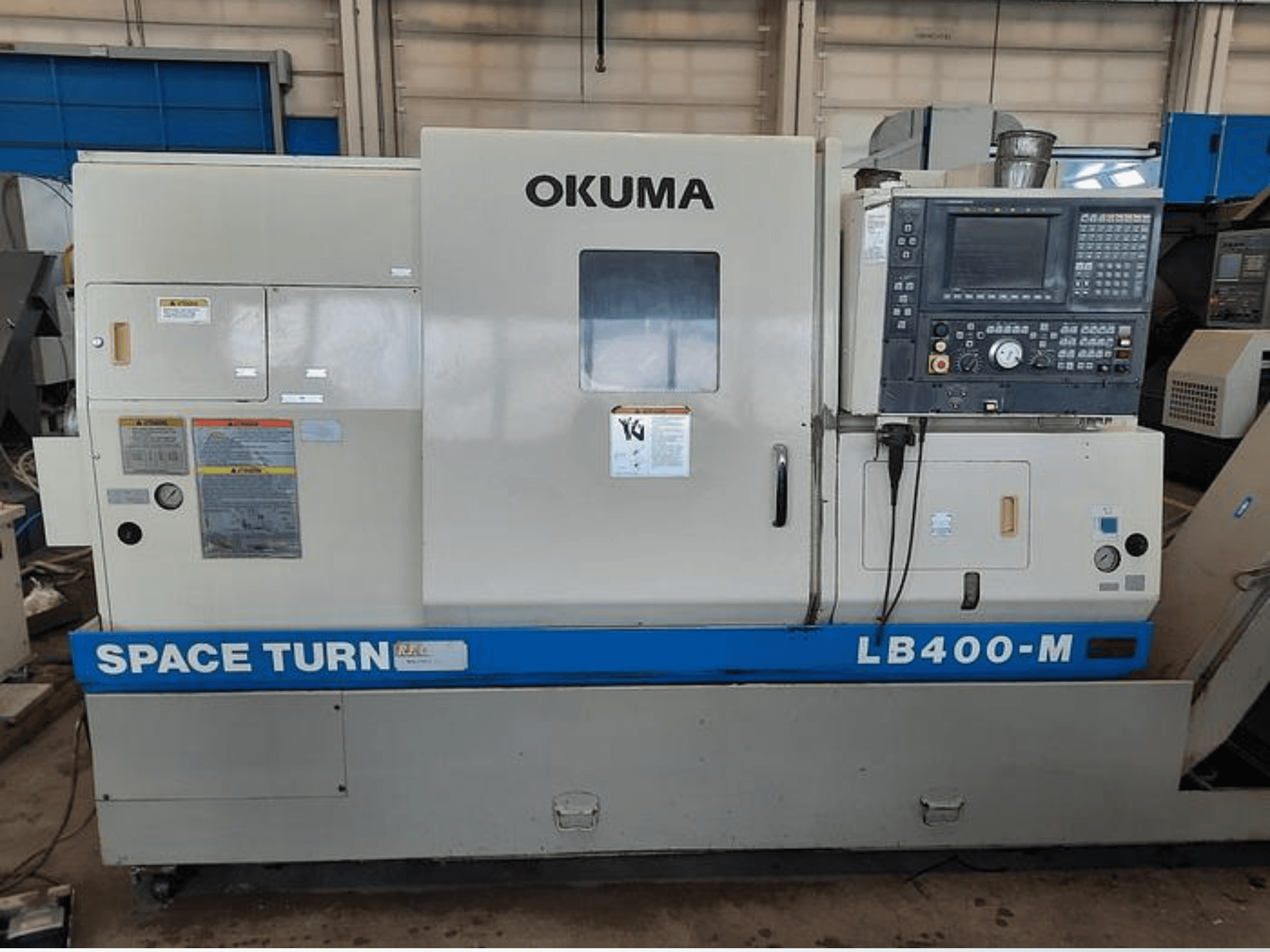 Okuma LB400-M CNC torna makinesi, kontrol paneli, uyarı etiketleri ve mavi "SPACE TURN" markası görünür şekilde önden görünüm.