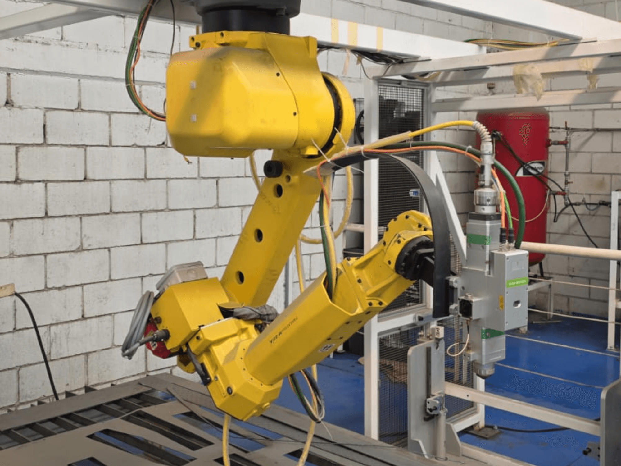 Birden fazla eklem ve kablo içeren hassas bir alete sahip sarı robotik kol, endüstriyel bir ortamda ön açıdan görüntülenmiştir.