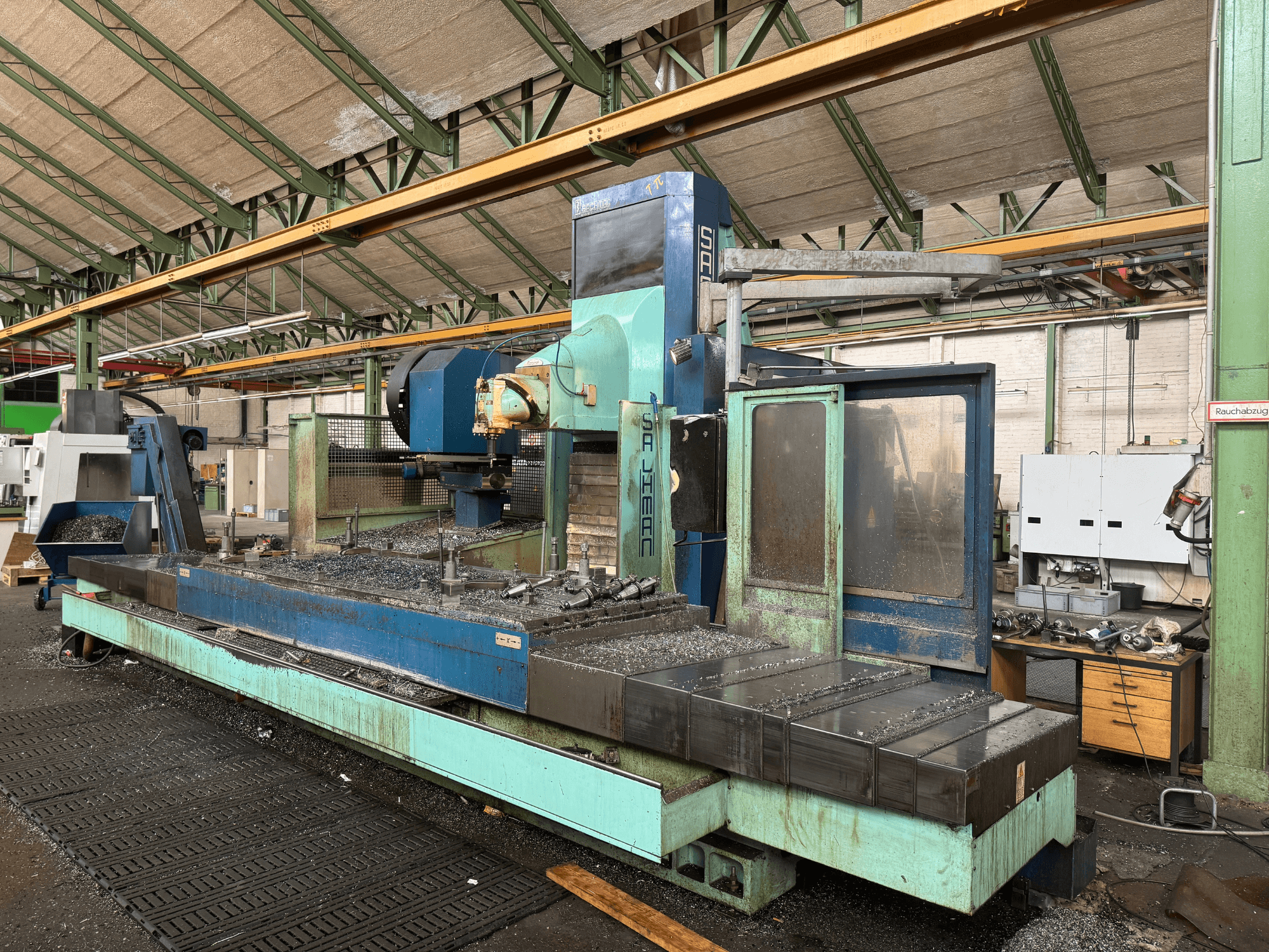 Fabrika ortamında Salvador freze makinesi, önden görünüm, mavi ve yeşil renk şeması, yataktaki metal talaşlarını gösteriyor.