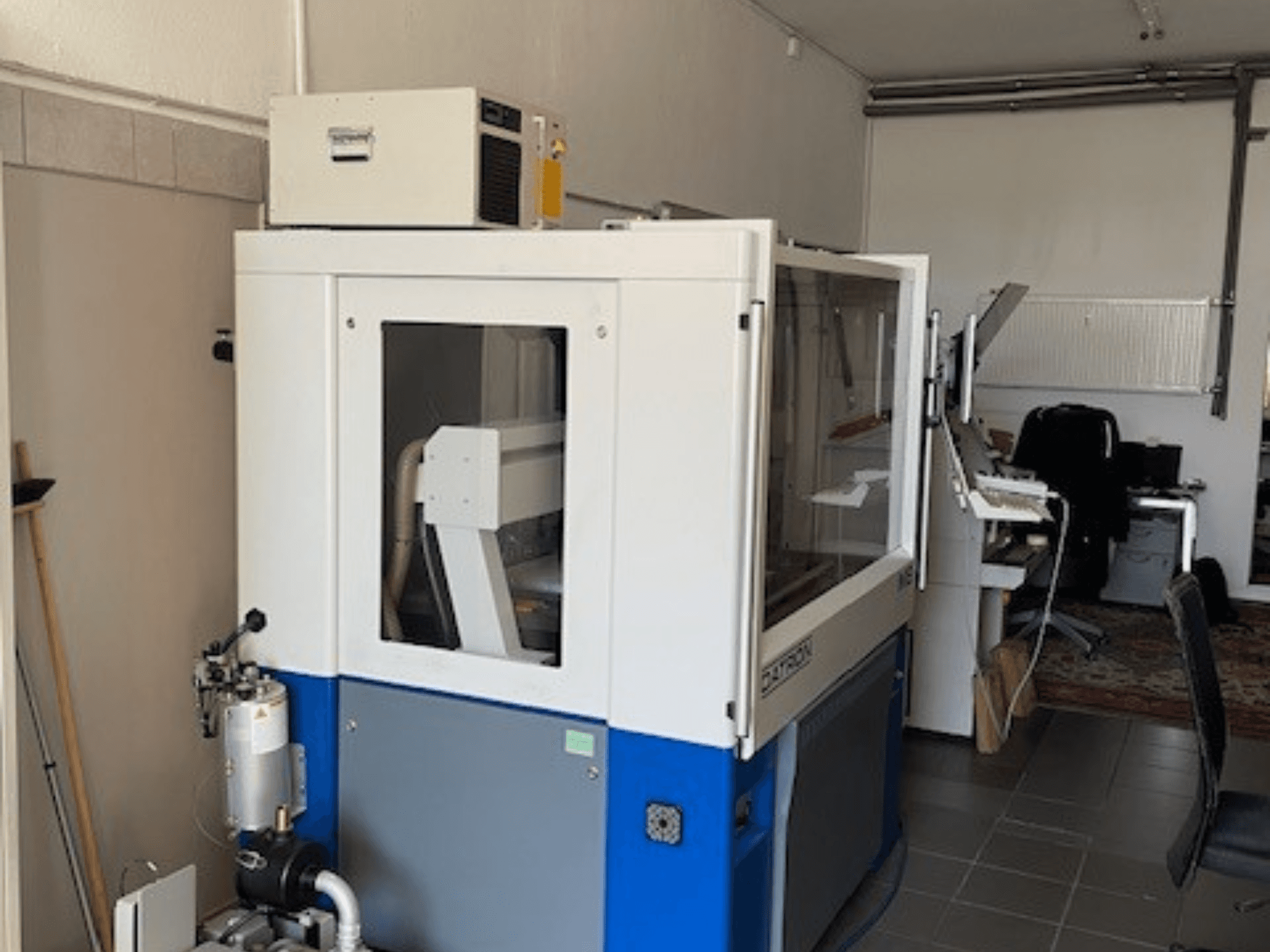 Şeffaf panelli, önden görünümlü, mavi ve beyaz endüstriyel makine, kontrol erişimi ve görünür havalandırma ünitesi içerir.
