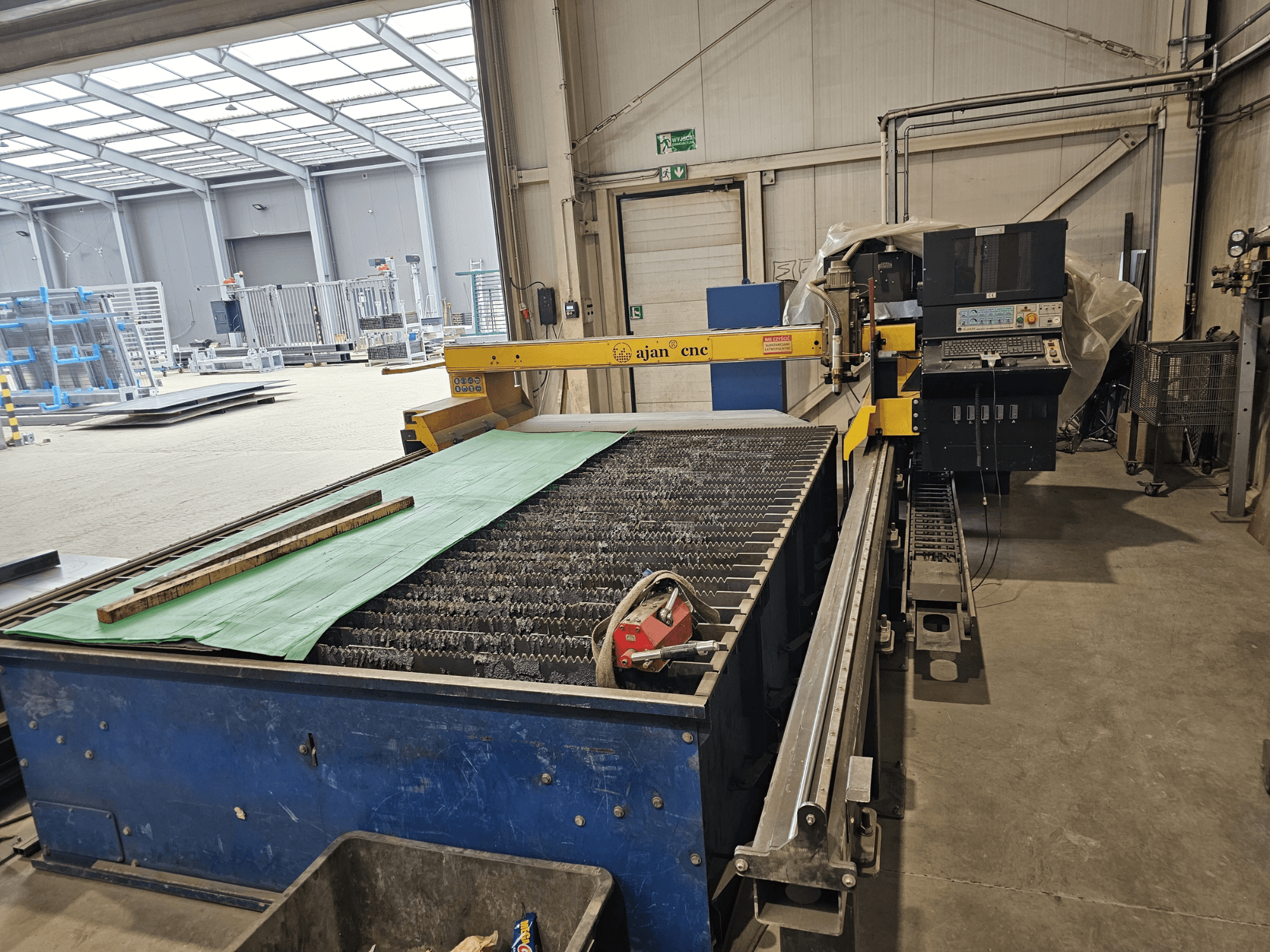 AJAN PP16011 Otomatik plazma kesme makinesinin yandan görünümü, atölye ortamında bir kesim masası ve kontrol paneline sahiptir.