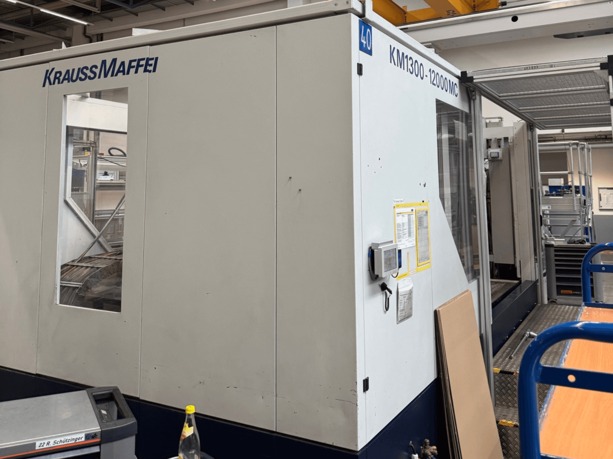Krauss Maffei Hidrolik Enjeksiyon Makinesi KM1300-12000 MC, yandan görünüm, kontrol paneli ve çalışma alanı.