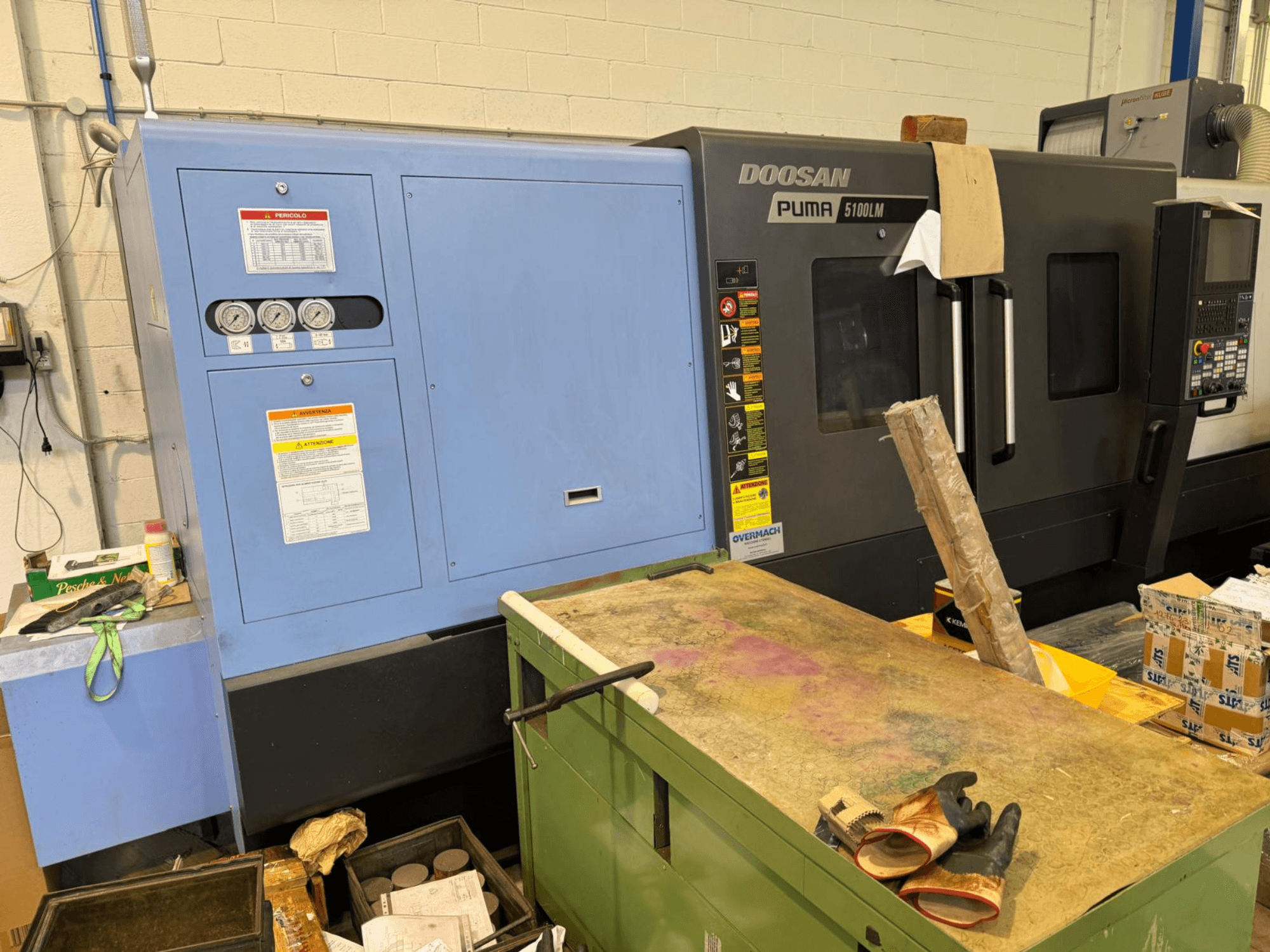 Doosan Puma 5100LM CNC makinesi ve kontrol paneli, yandan görünüm. Göstergeler ve uyarı etiketleri mavi kontrol ünitesinde görülebilir.