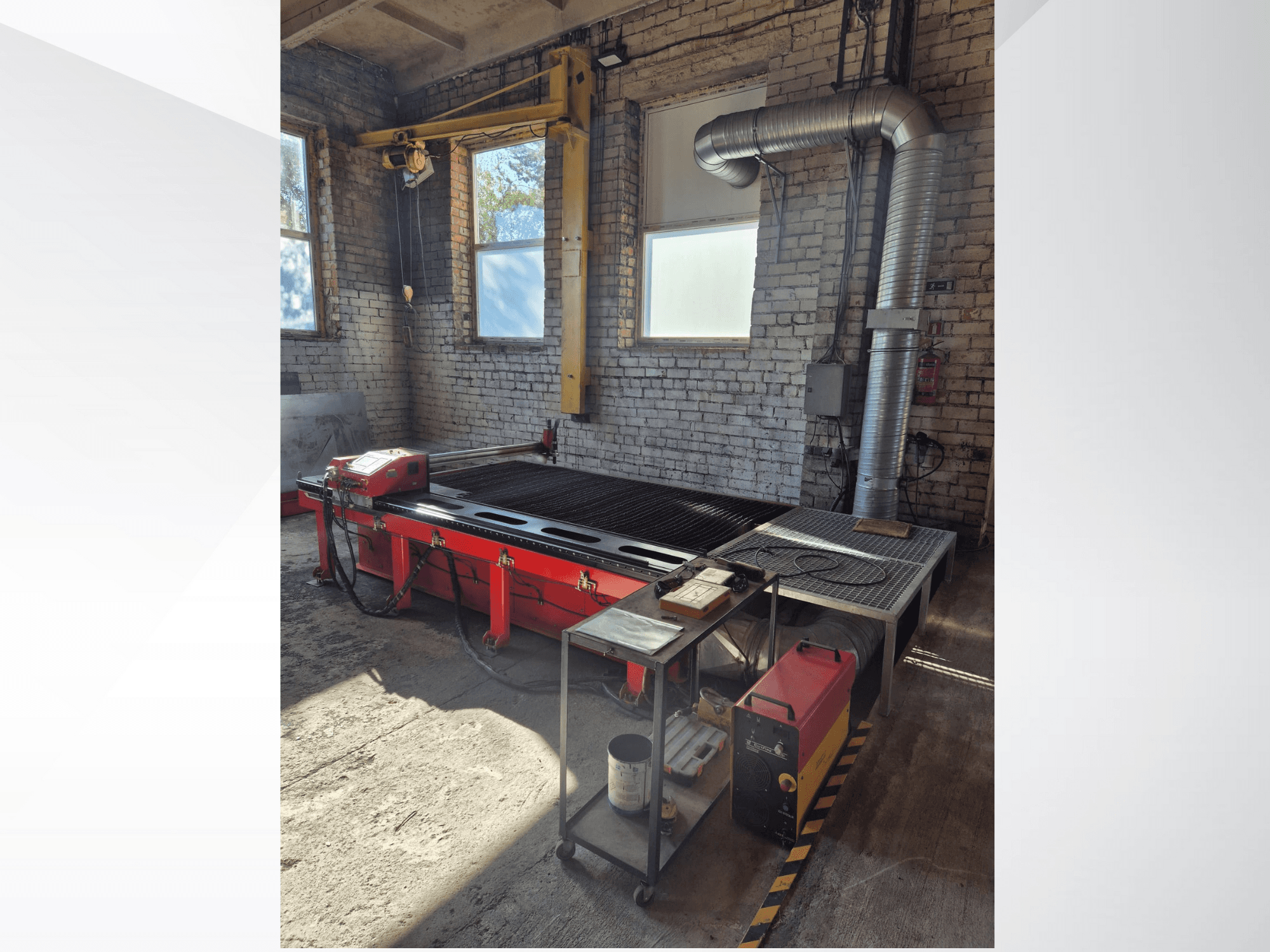 İyi aydınlatılmış bir atölyede yandan bakıldığında kontrol paneli ve metal egzoz kanalı bulunan kırmızı CNC plazma kesim masası.