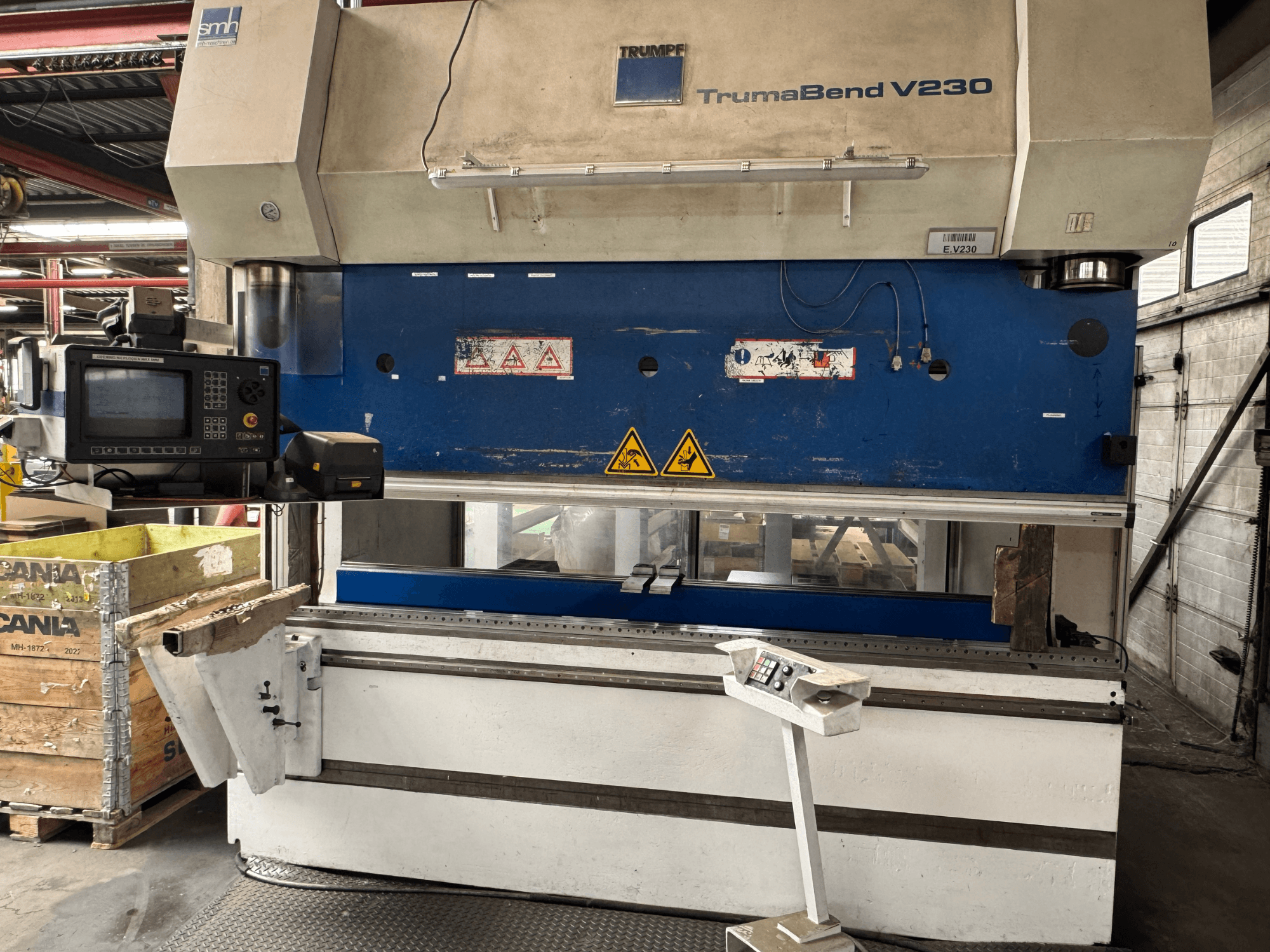 TRUMPF TrumaBend V230 abkant pres, kontrol paneli, uyarı etiketleri ve iş parçası destek kolu görünür şekilde önden görünüm.