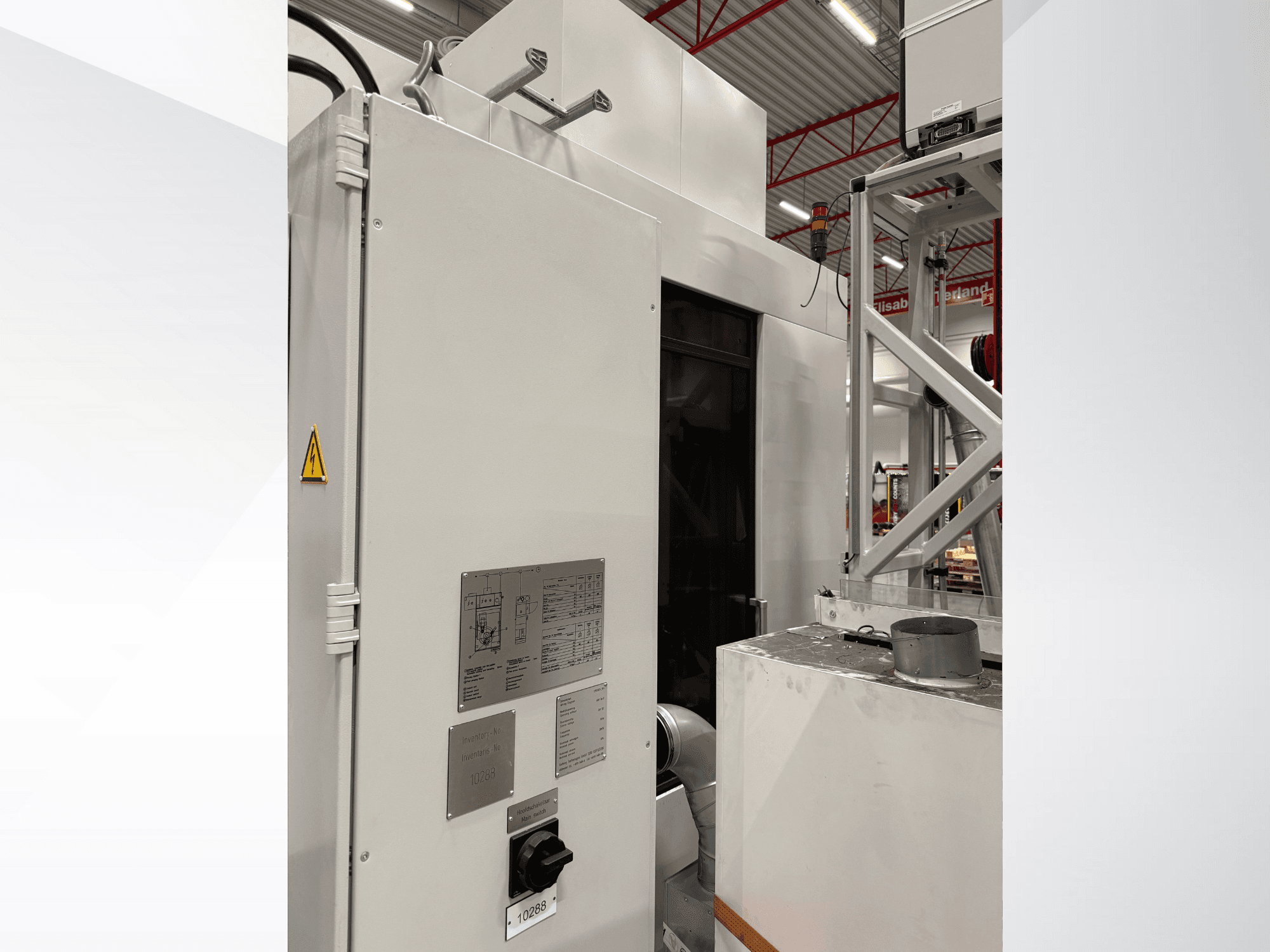 Otomatik bir sistemin parçası olan, kontrol paneli ve uyarı etiketi bulunan beyaz bir endüstriyel makinenin yandan görünümü.