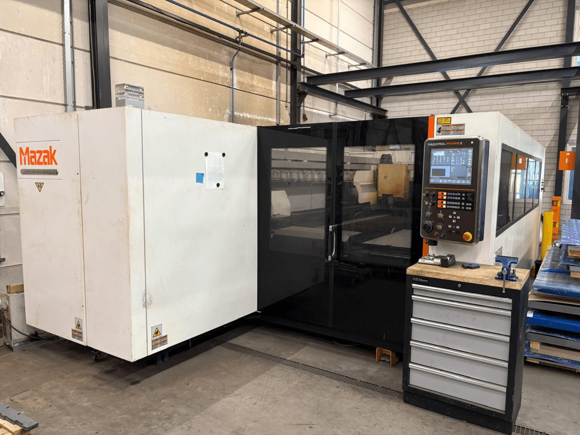 Mazak Optiplex 3015 CO₂ lazer kesim makinesi, önden görünüm; kontrol paneli ve endüstriyel ortam gösterilmektedir.