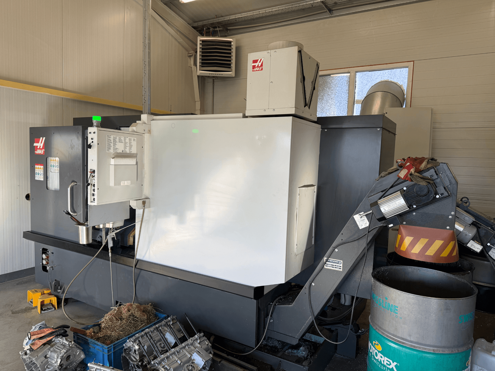 Kontrol panelli Haas CNC makinesi, yandan görünüm; görünür soğutma sıvısı ve yağ hatları; mavi kutuda metal hurdalar; endüstriyel ortam.