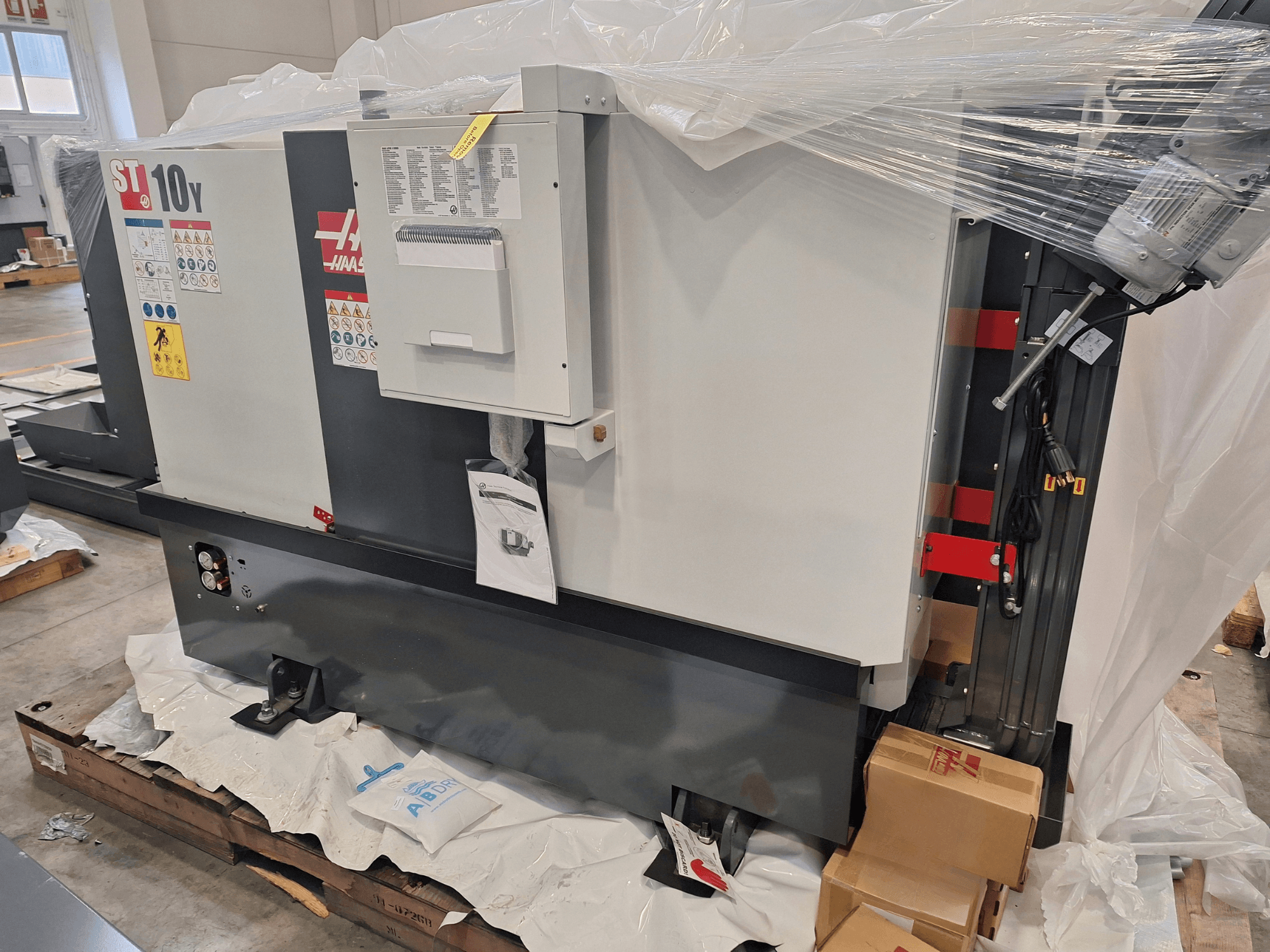 HAAS ST-10Y EU yatay torna tezgahının yandan görünümü; plastik ambalajlı, kontrol paneli ve uyarı etiketleri görünür durumda.