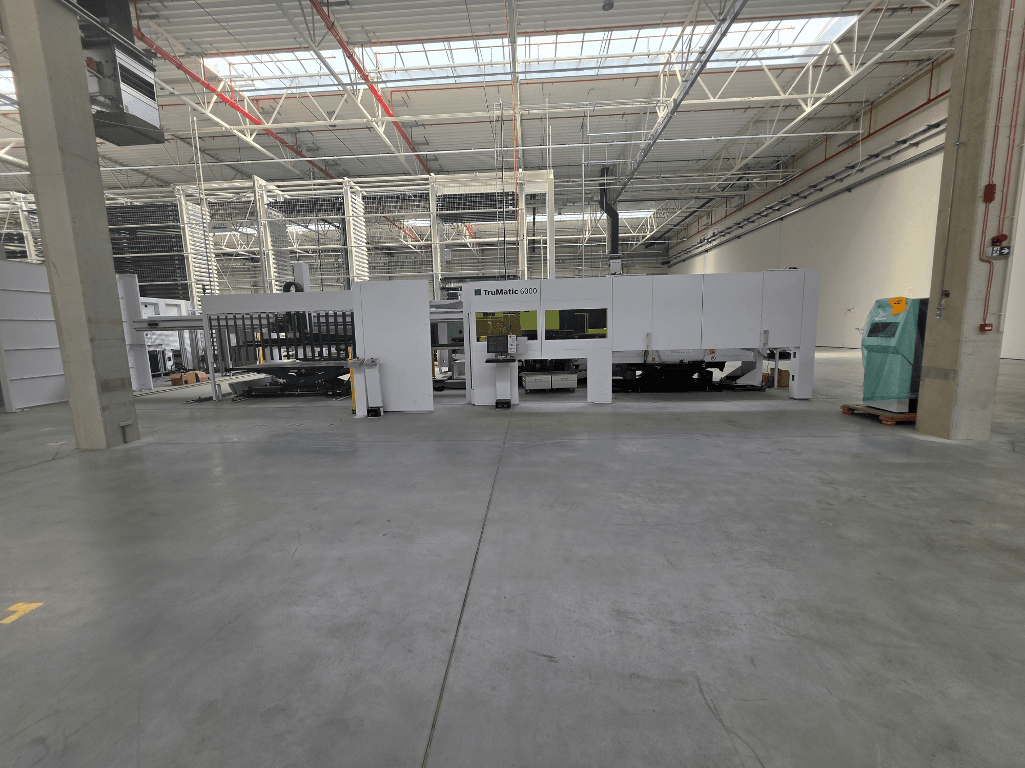 Geniş bir depo içinde bulunan TRUMPF TruMatic 6000-1600 fiber delme-lazer kombine makinesi, önden görünüm.