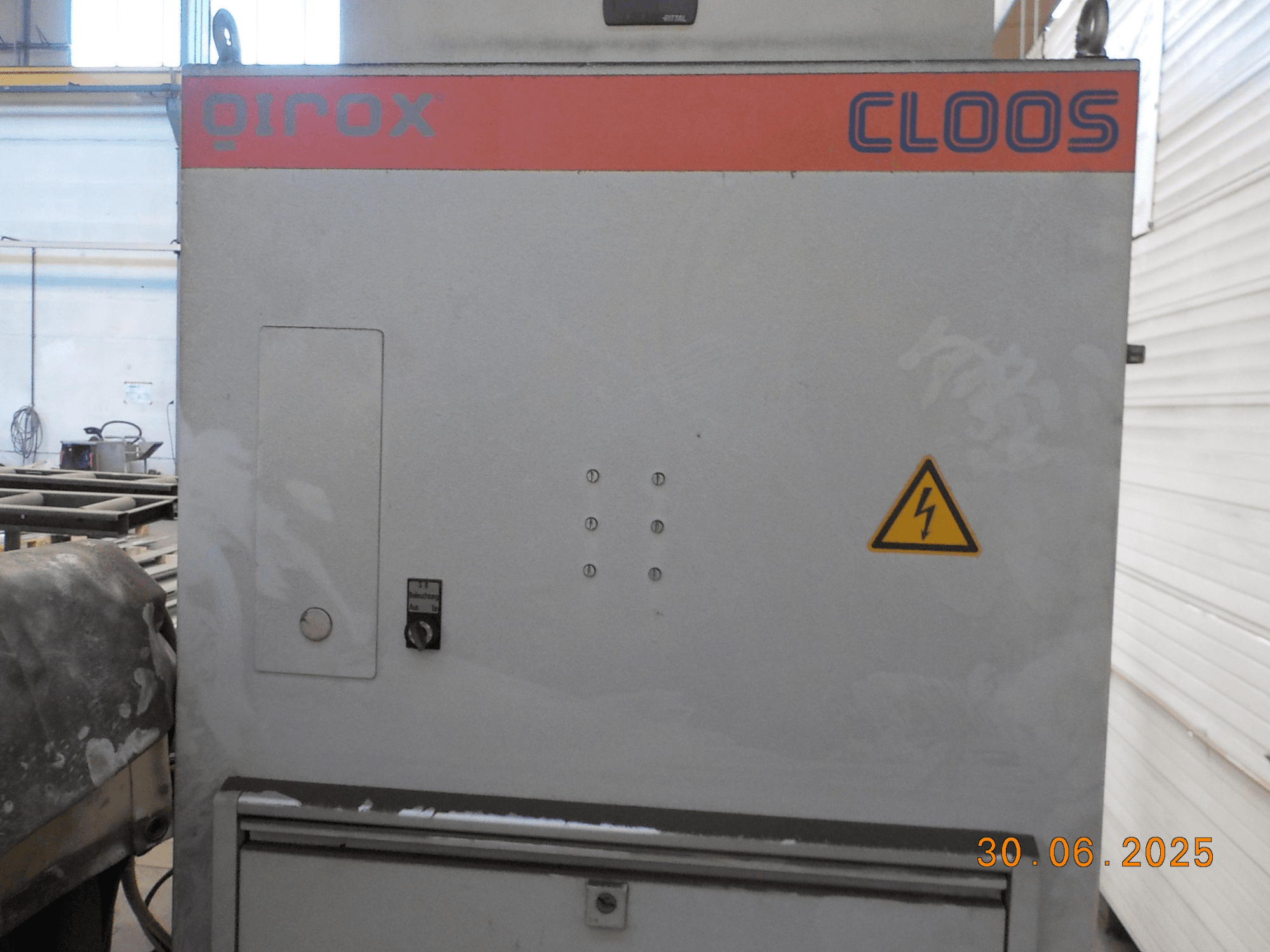 Cloos QIROX kaynak makinesinin yandan görünümü, kontrol paneli ve uyarı işareti, tozlu bir yüzey ve görünür tarih damgası.