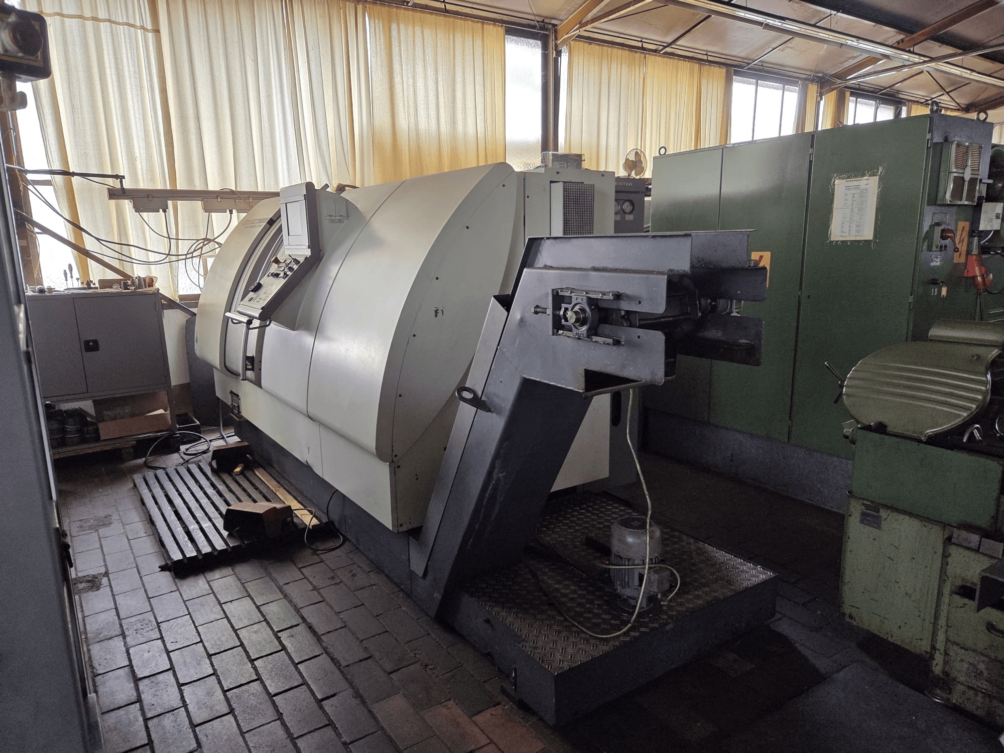 Gildemeister CTX 400 çift işleme merkezi, yandan görünüm; kontrol paneli, geniş şasi ve atölyedeki bitişiğindeki makineleri göstermektedir.