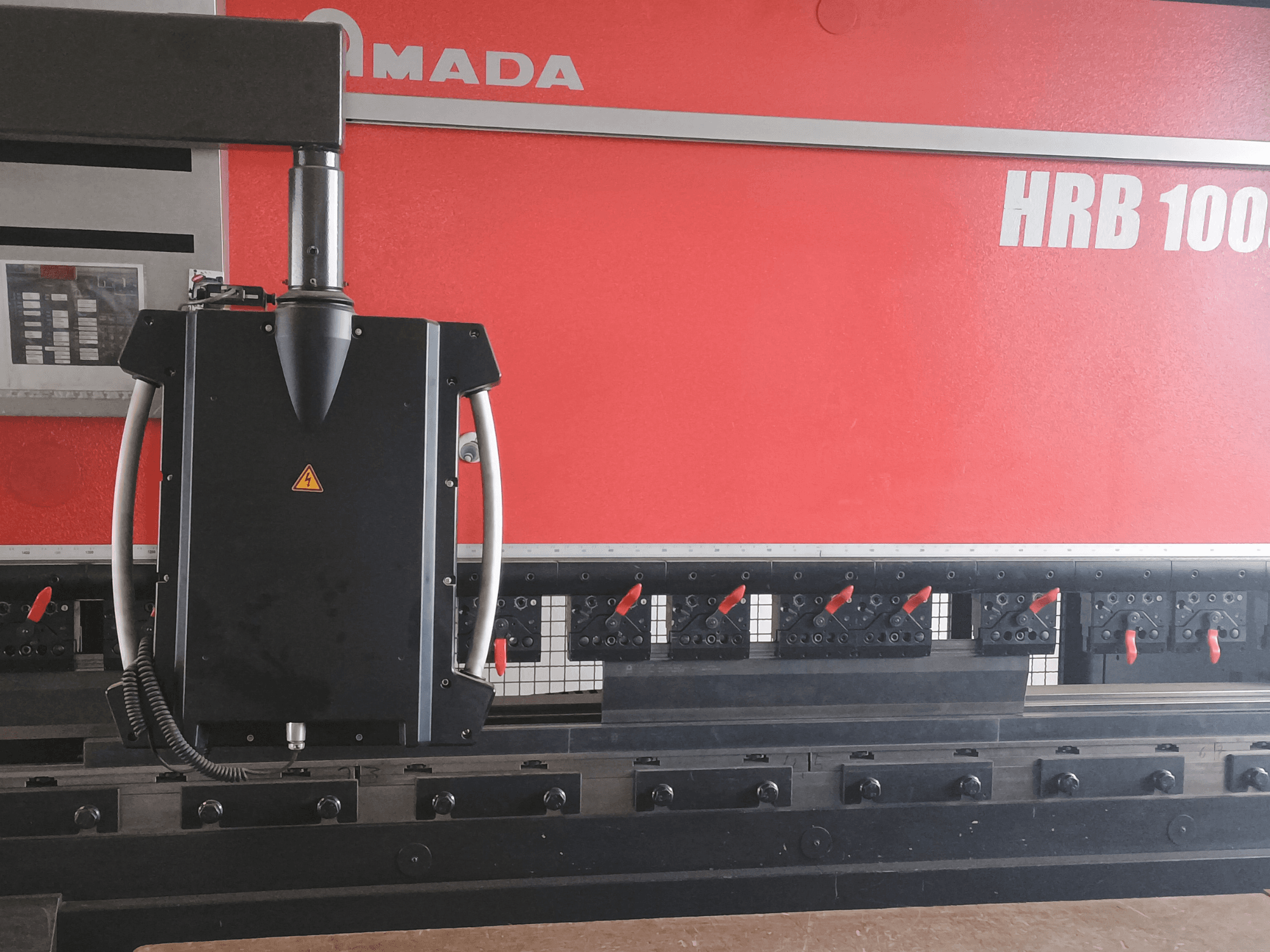 Amada HRB 100 bükme makinesi önden görünüm; konik nozullu ve ayarlanabilir kelepçeli siyah bir kontrol kafasına sahiptir.