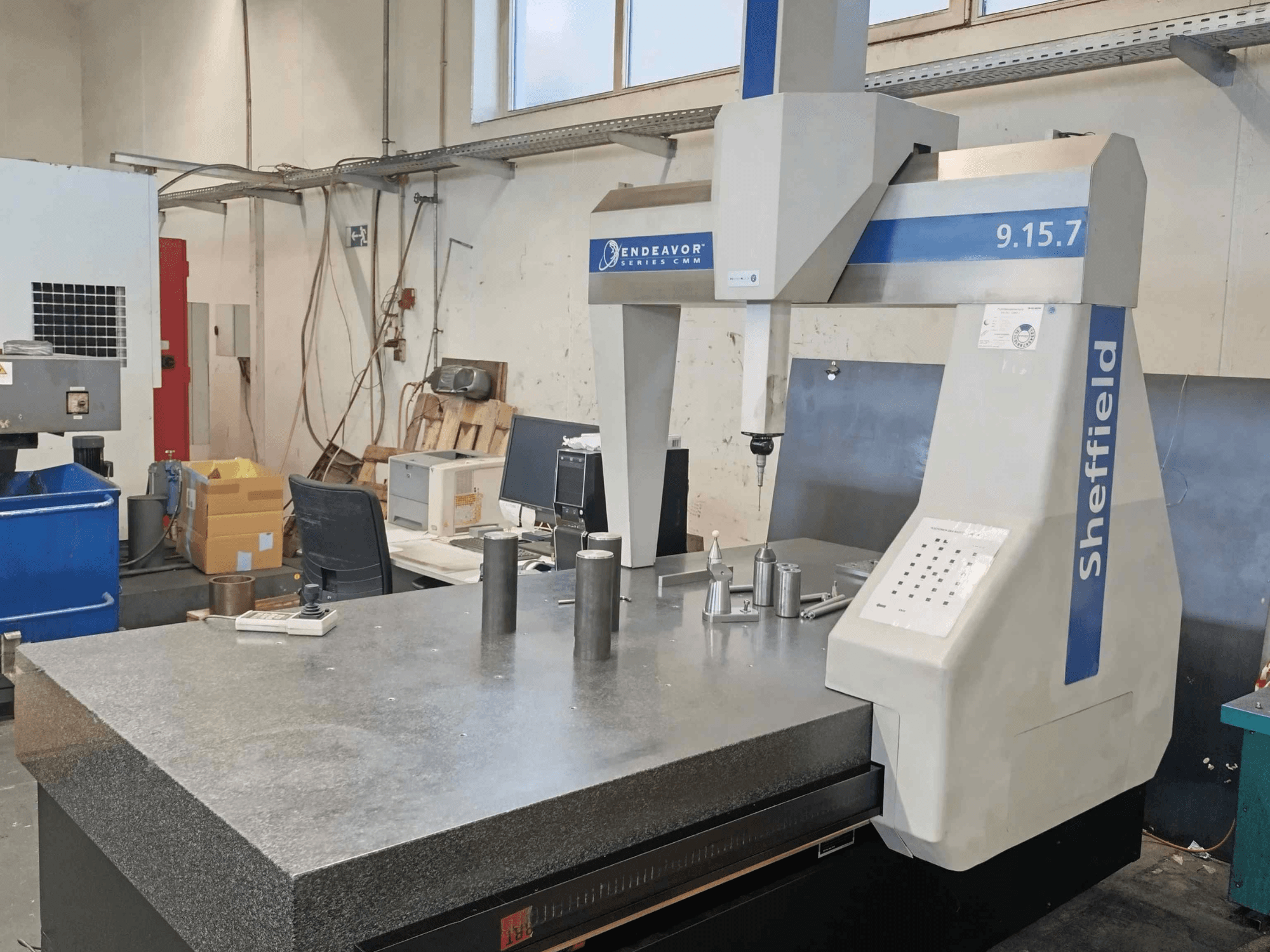 Koordinat Ölçüm Makinesi Sheffield Endeavor 9.15.7, granit bir masa ve metalik iş parçalarının bulunduğu bir atölyede.