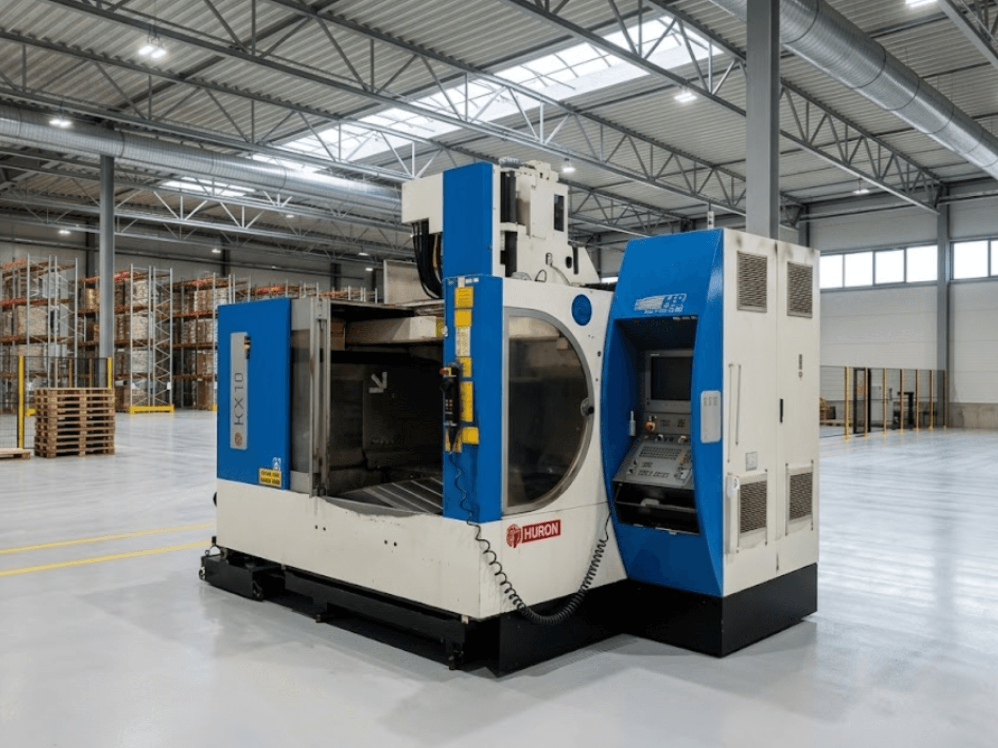 Bir depoda bulunan Huron KX 10 dikey işleme merkezi; kontrol paneli ve açık çalışma alanını gösteren yandan görünüm.