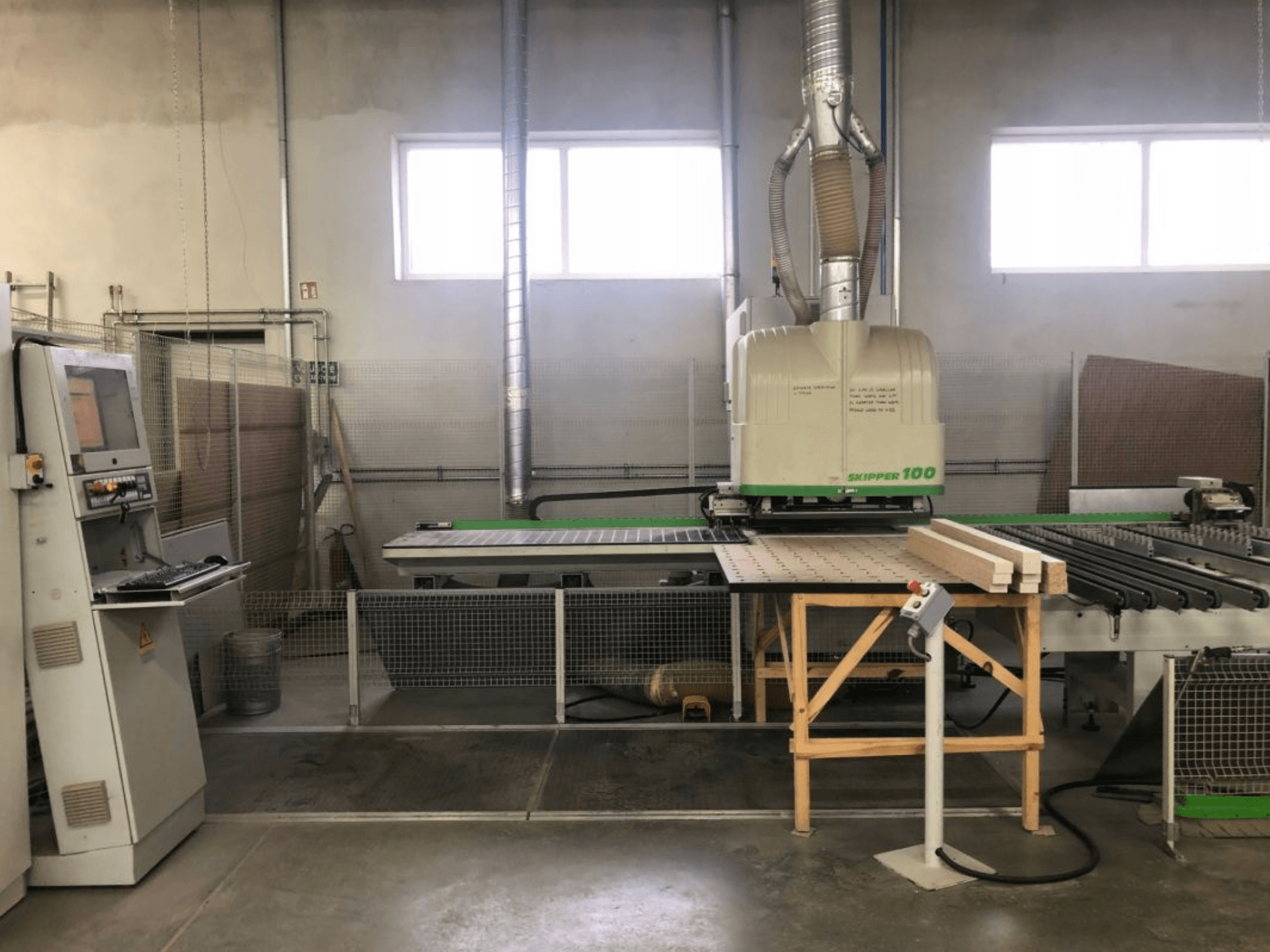 Bir atölyede bulunan BIESSE SKIPPER 100 CNC işleme merkezi; önden bakıldığında, kontrol paneli ve çalışma masası üzerinde ahşap bulunan makine görülmektedir.
