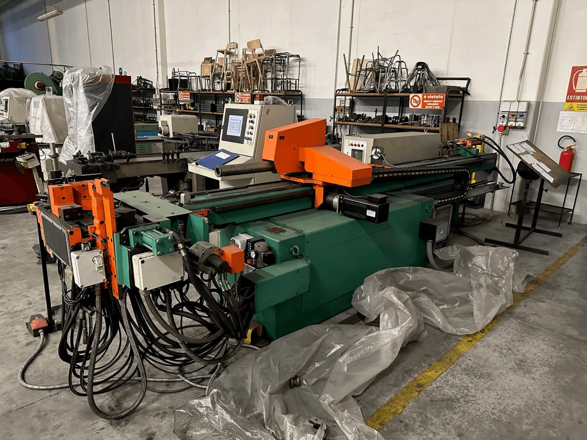 Bir atölye ortamında önden bakıldığında turuncu ve yeşil gövdeli, kontrol panelli ve çok sayıda kabloya sahip endüstriyel makine.