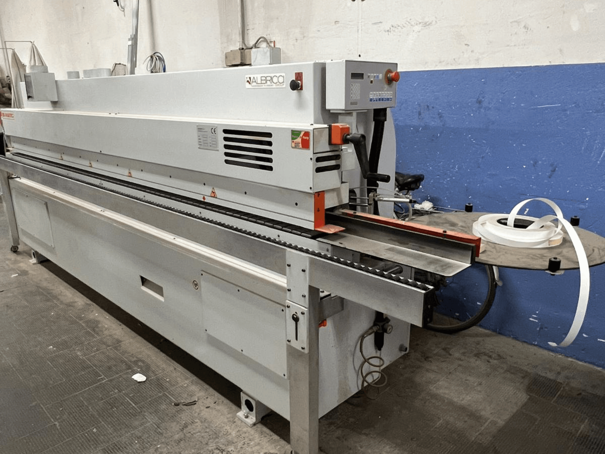 Önden görünümlü ALBRICO kenar bantlama makinesi, uzun bir konveyör bandı ve ekli bir yapışkan bant rulosu içerir.