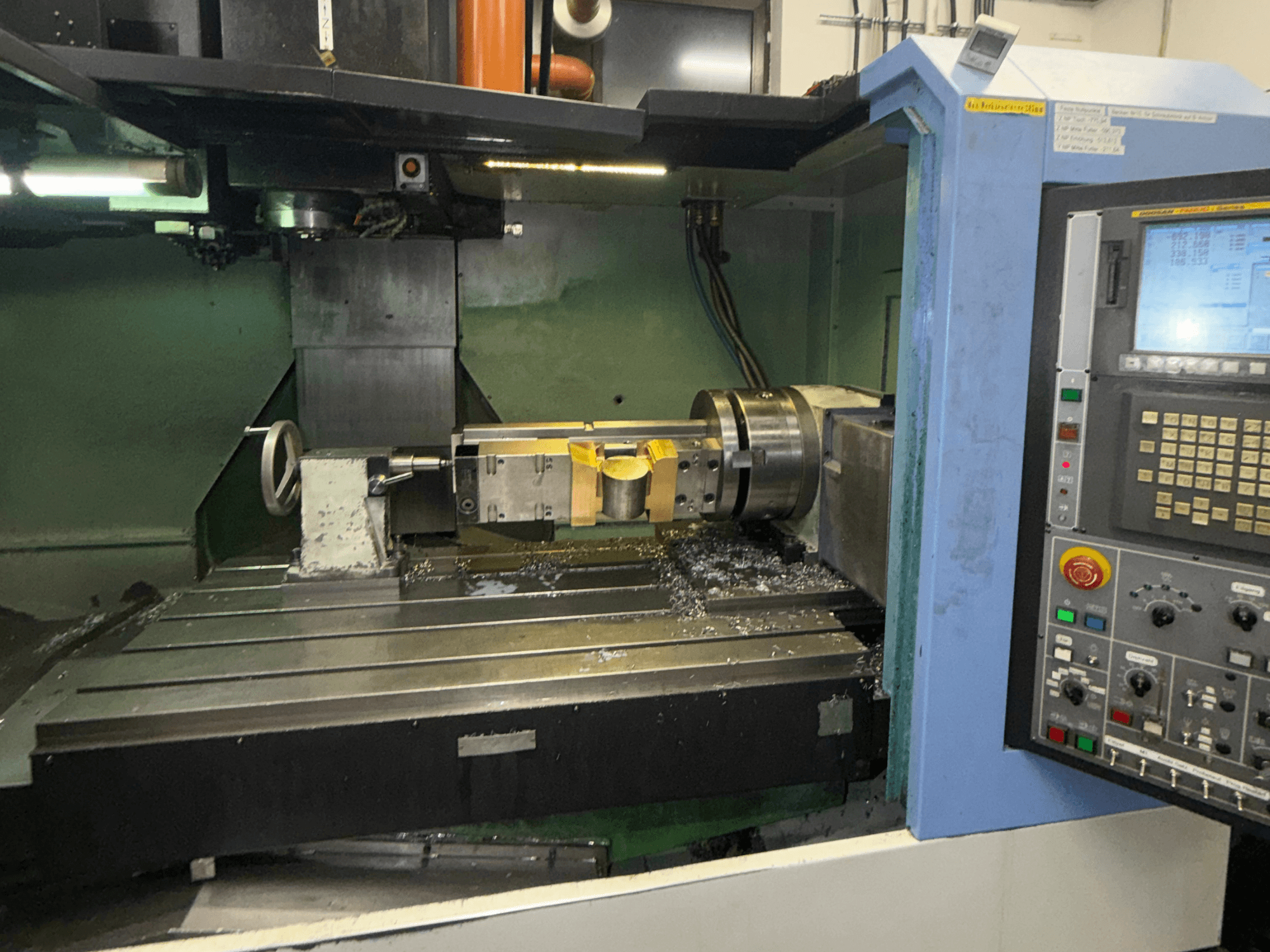 DOOSAN DNM650 Dikey İşleme Merkezi, önden görünüm; kesici takım ve kontrol paneli görülmekte olup, tezgah üzerinde metal talaşları da göze çarpmaktadır.