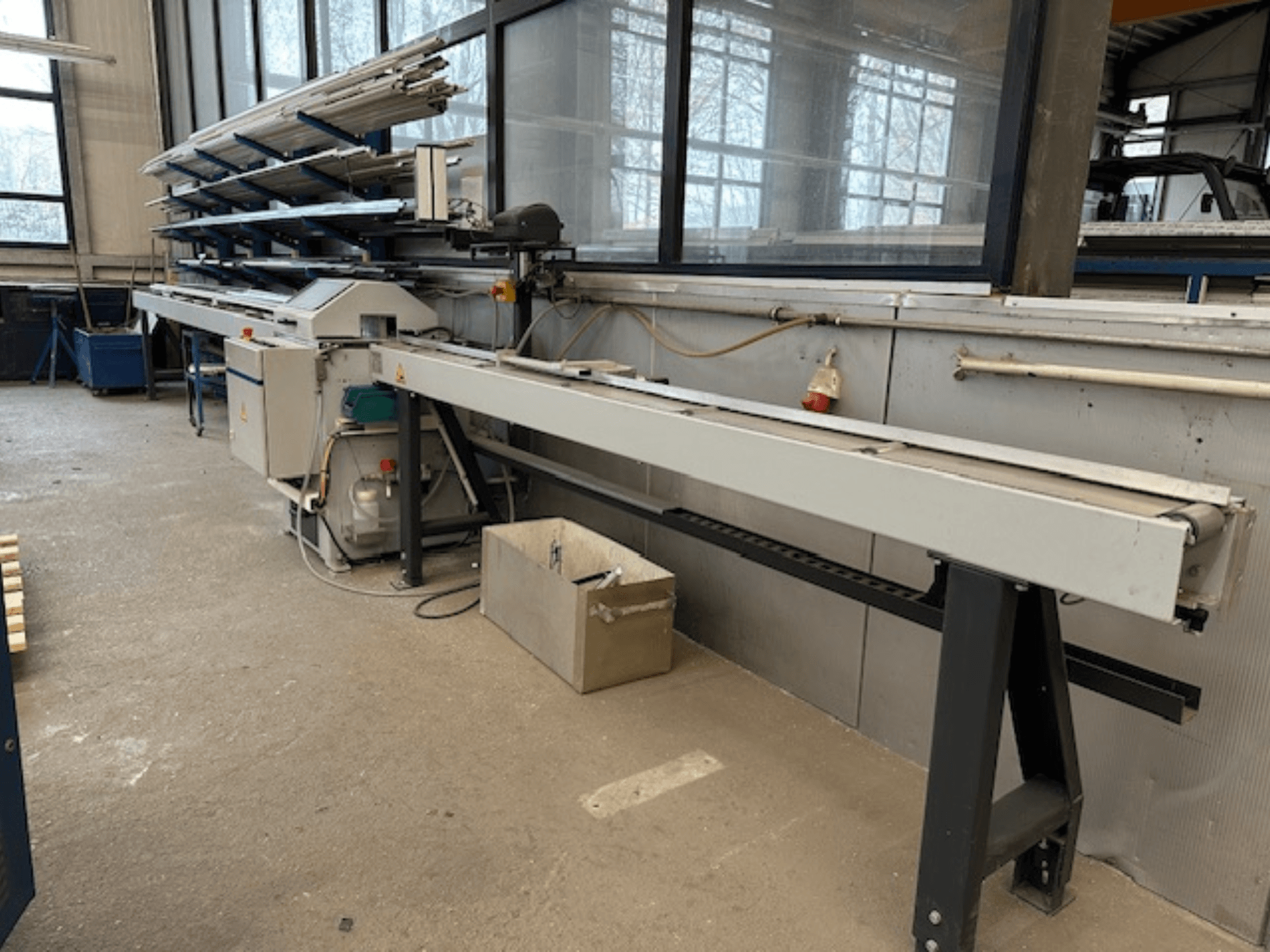 SCHÜCO PGS Dairesel Metal Testeresi atölyede, ayarlanabilir kesme yatağı ve üzerinde metal profil rafı ile yandan görünüm.