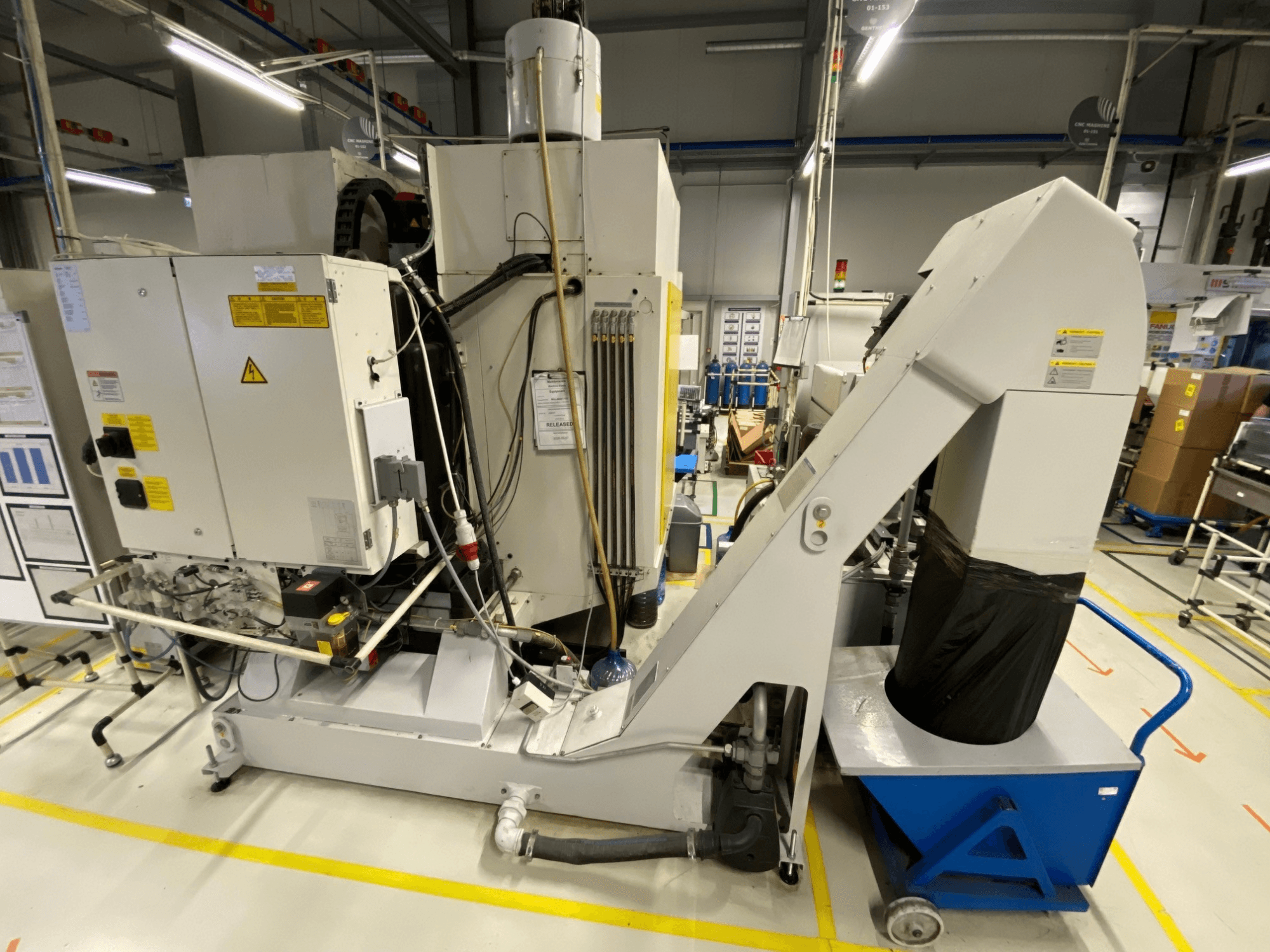 FANUC ROBODRILL α-D21LiB dikey işleme merkezinin önden görünümü; elektrikli bileşenler ve çıkış oluğu gösterilmektedir.