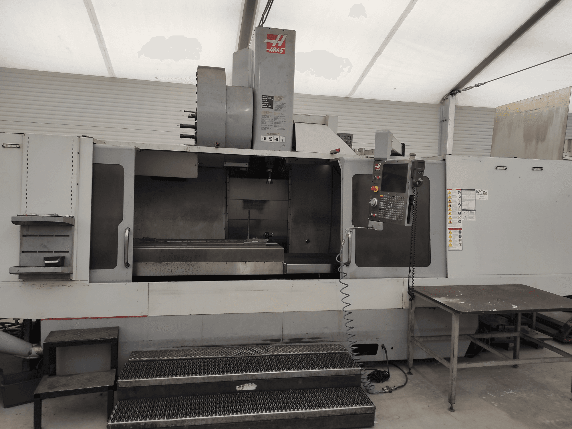 HAAS VF-10/50HE Dik İşleme Merkezi, kontrol panelini, makine yatağını ve çalışma için erişilebilir basamağı gösteren önden görünüm.