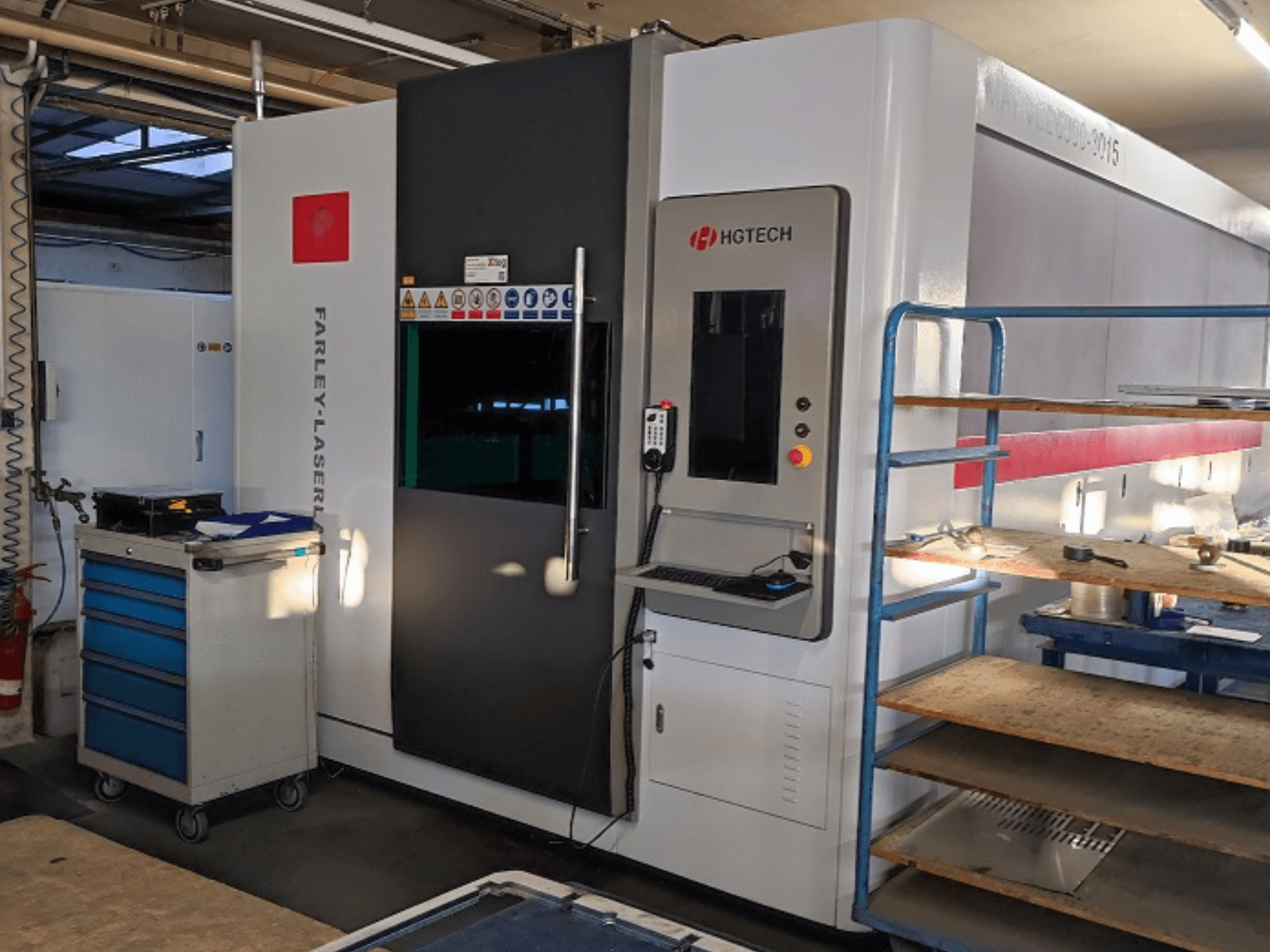 HGTECH Marvel 6000-3015 fiber lazer kesim makinesi, kontrol paneli ve bitişik depolama ile önden görünüm.
