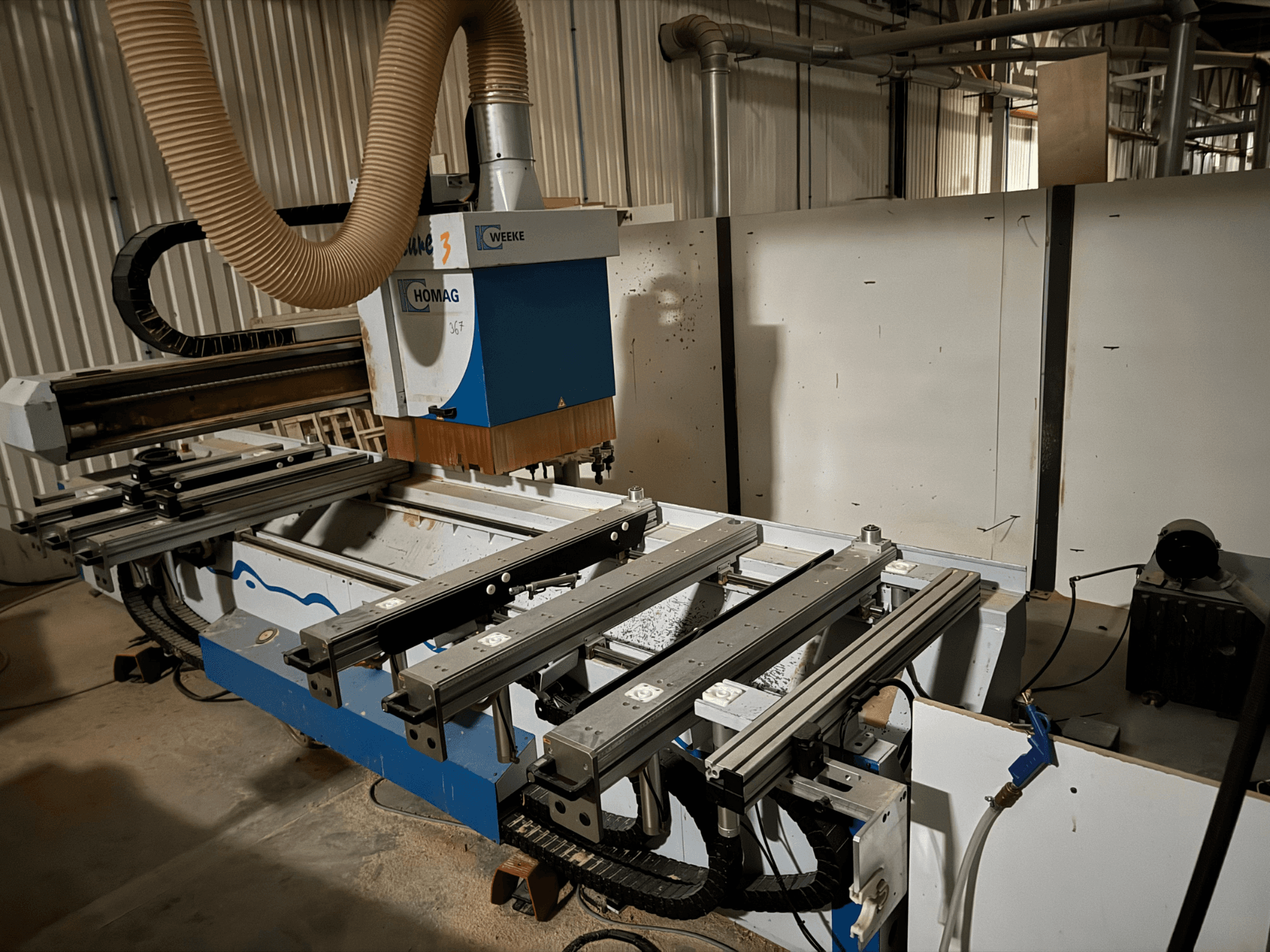 Mavi ve beyaz tasarımlı HOMAG CNC makinesi, yandan görünüm, kayar raylar, toz emme sistemi ve monte edilmiş takımlara sahiptir.