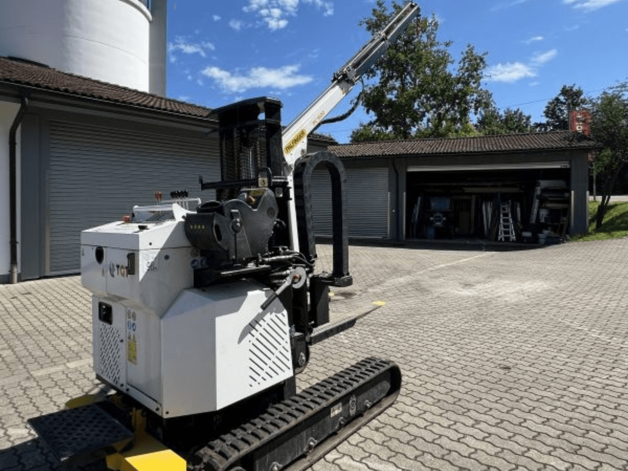 TGI inşaat mini vinci, yandan görünüm, rayları ve monte edilmiş bomu sergiliyor, bir garajın yanında tuğla bir yüzeye park edilmiş.