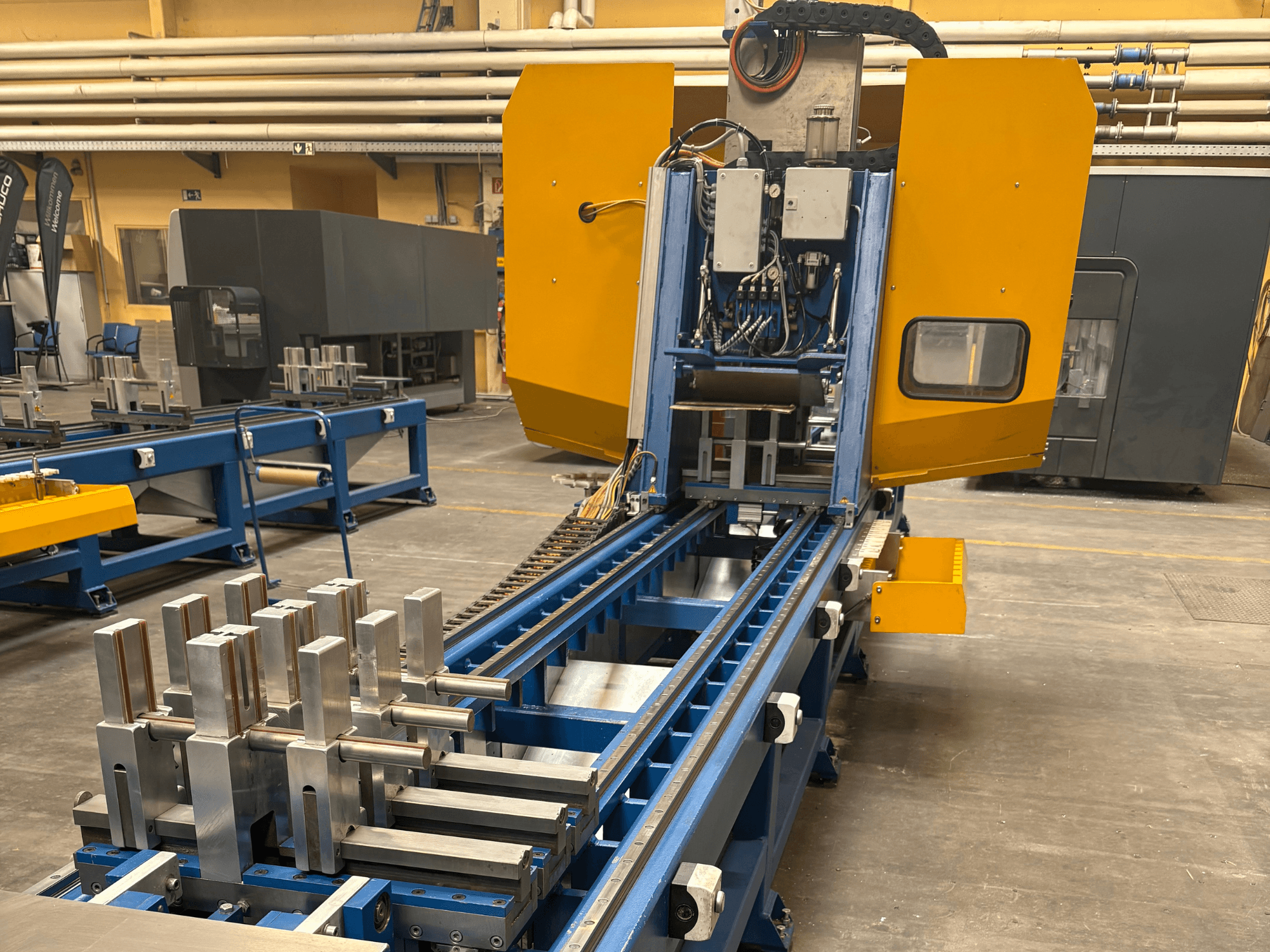 SCHÜCO PBX AL Üniversal İşleme Merkezi'nin önden görünümü, mavi işleme yatağı üzerinde metalik iş parçalarını sergiliyor.