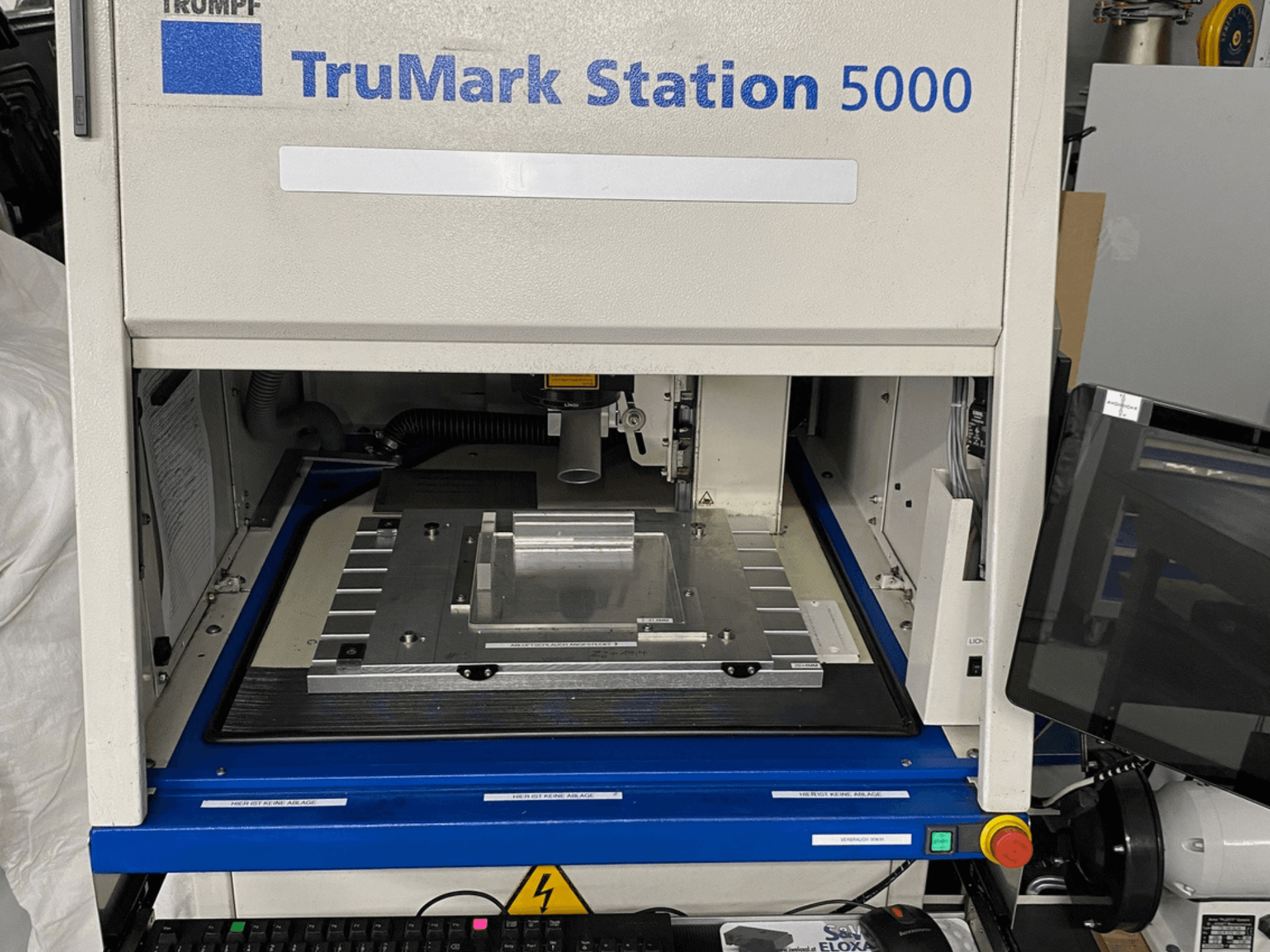 TruMark Station 5000 lazer markalama makinasının önden görünümü; çalışma masasını, kumandaları ve izleme ekranını gösterir.