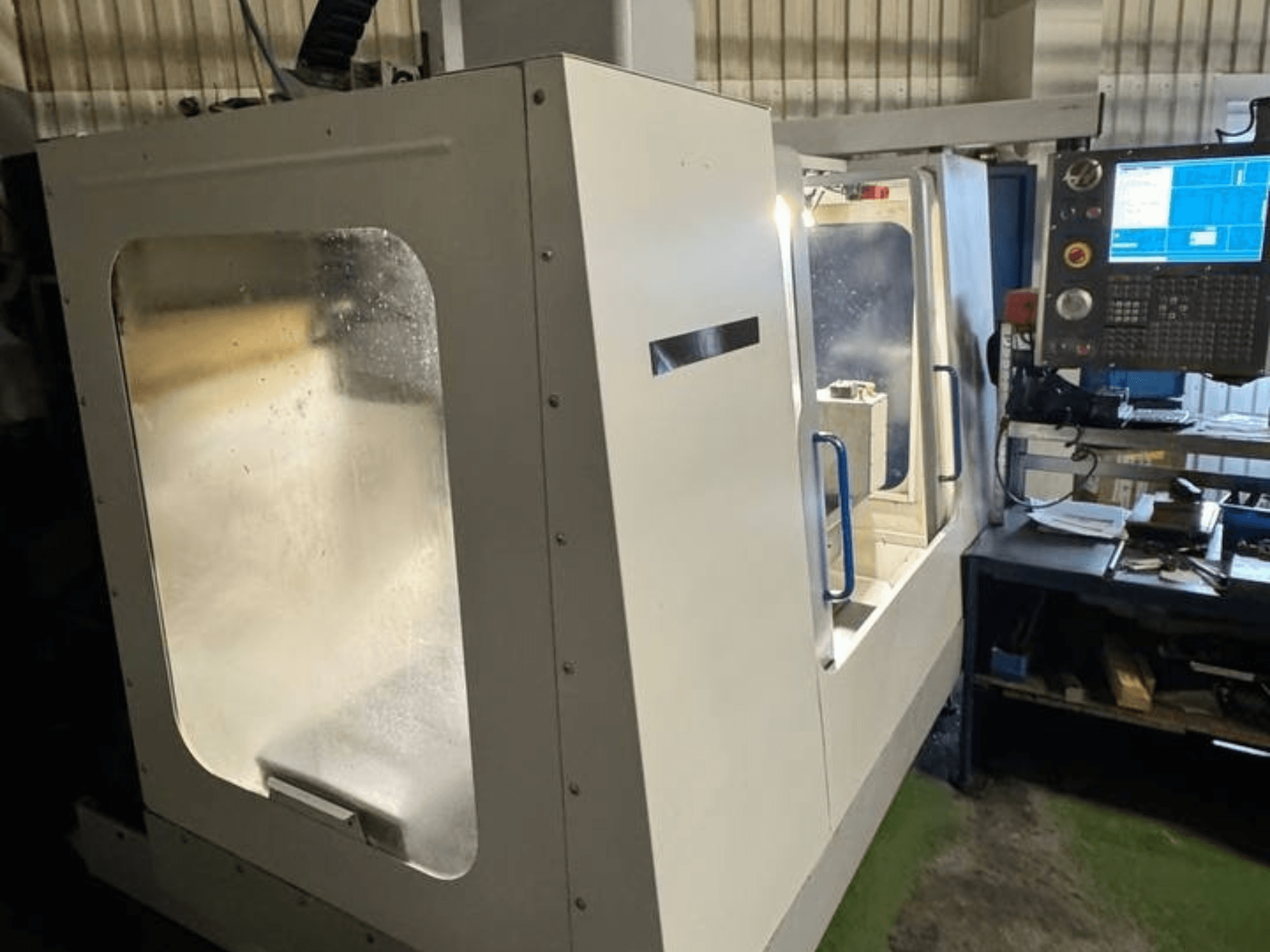 HAAS VCE 750 Dik İşleme Merkezinin yandan görünümü, kontrol paneli ve şeffaf güvenlik muhafazası.