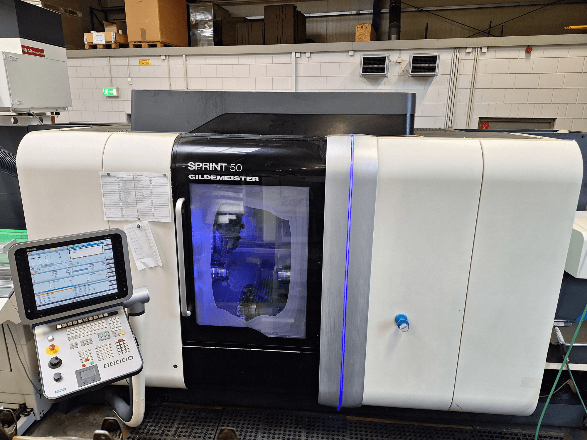 DMG Sprint 50 2T yatay tornalama makinesi, önden görünüm, kontrol paneli ve içindeki makineleri sergileyen şeffaf muhafaza.